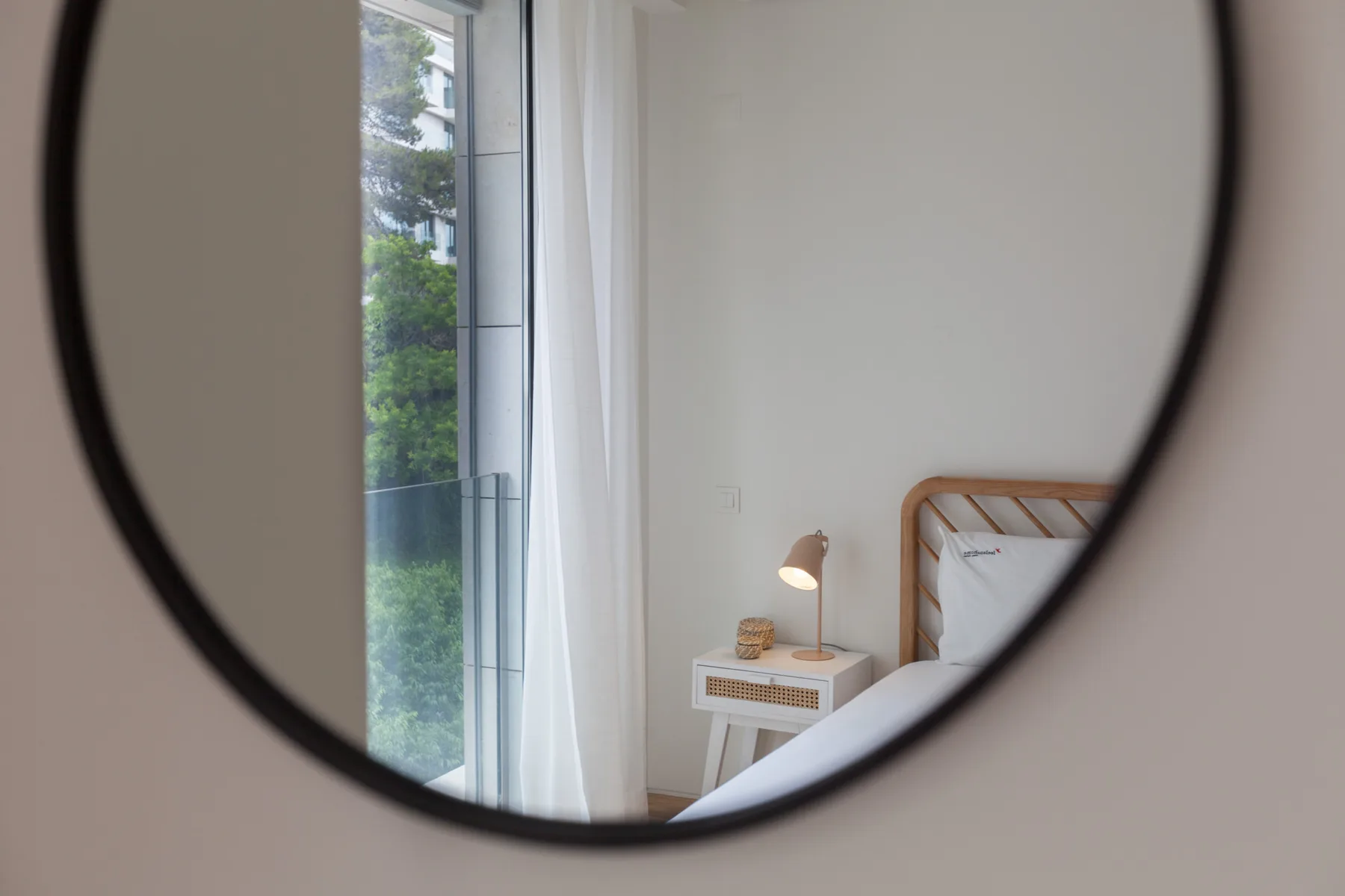 A bedroom with a bed beside a tall window and a small bedside table.