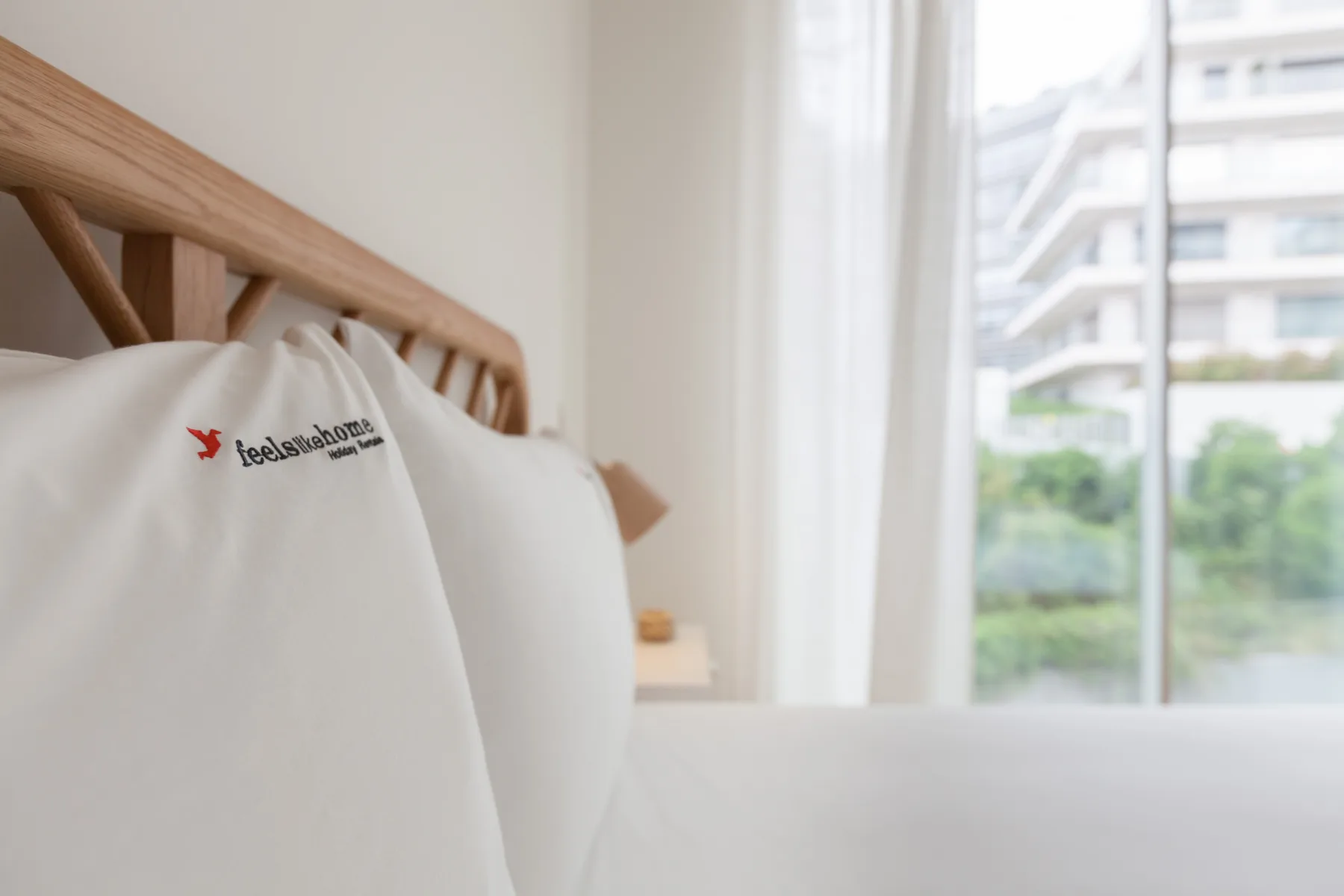A bedroom with white bedding, a wooden headboard, and a large window.