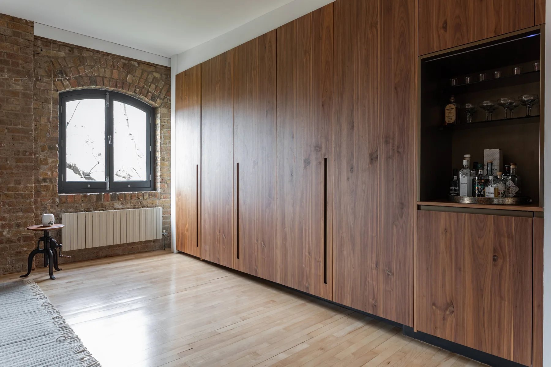 A wood-paneled room with a large built-in cabinet beside a brick wall and window.