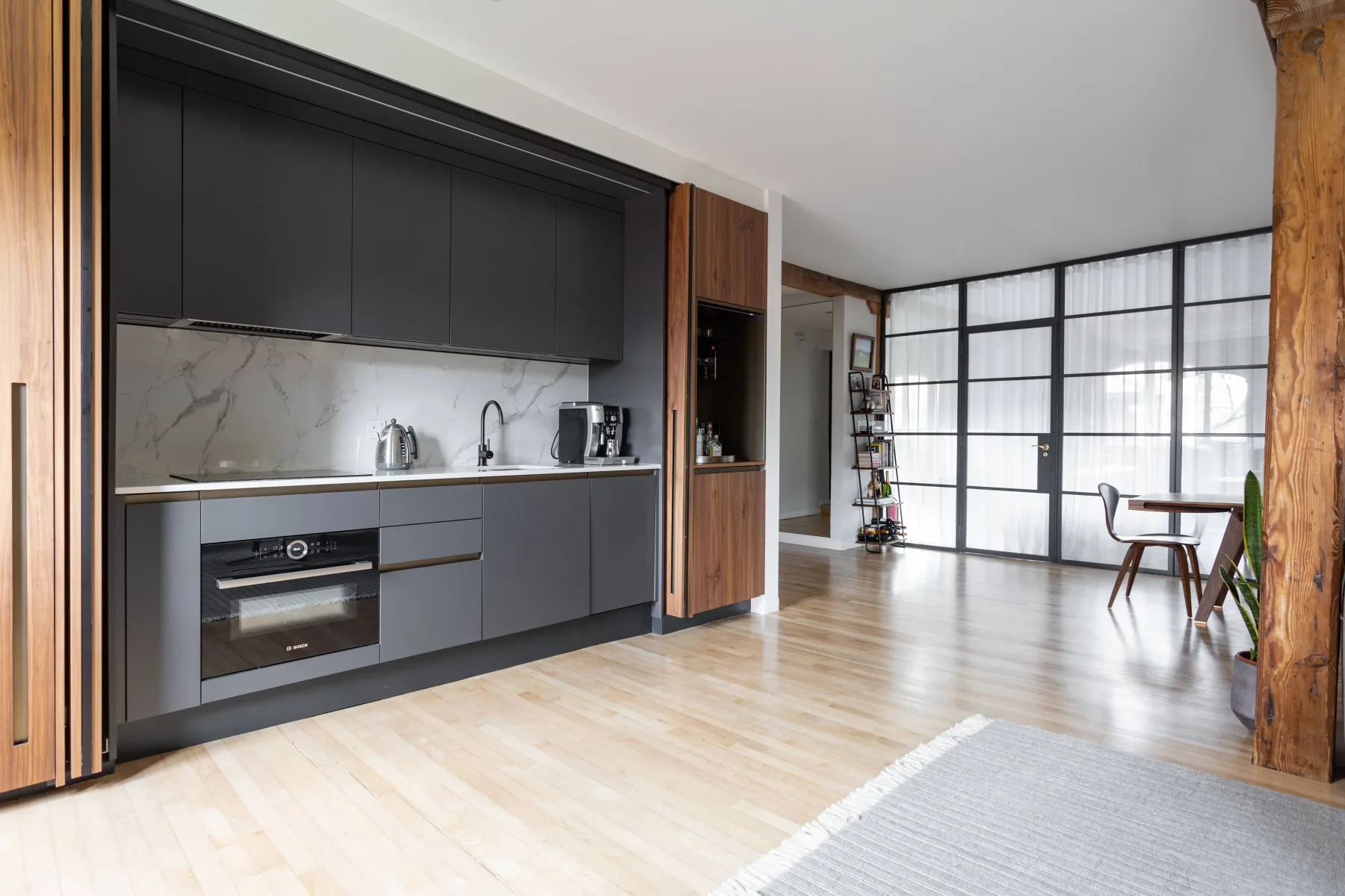A modern kitchen opens onto a dining area beside large grid windows.