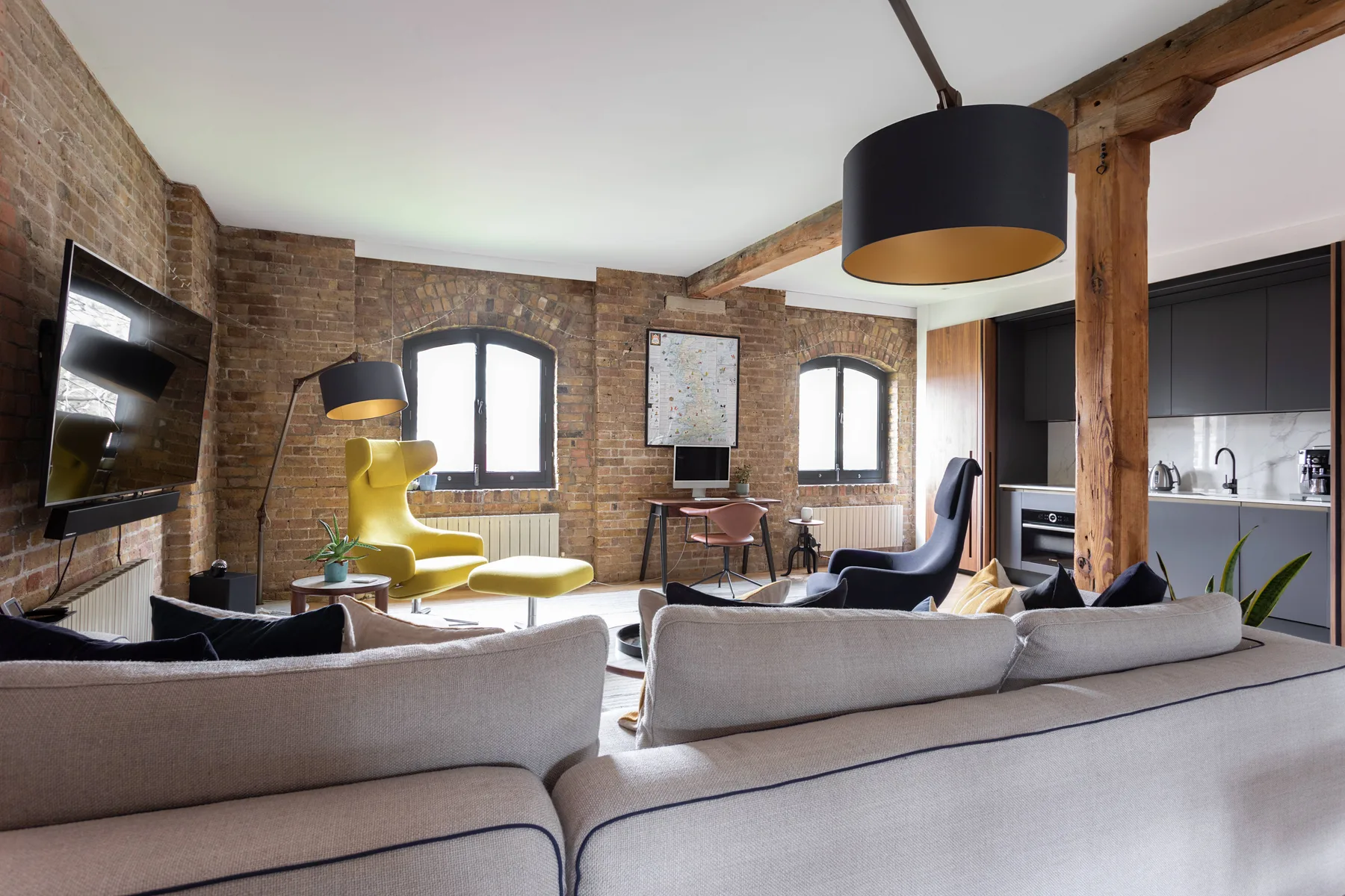 A brick-walled living room with seating, a television, and a compact kitchen area.
