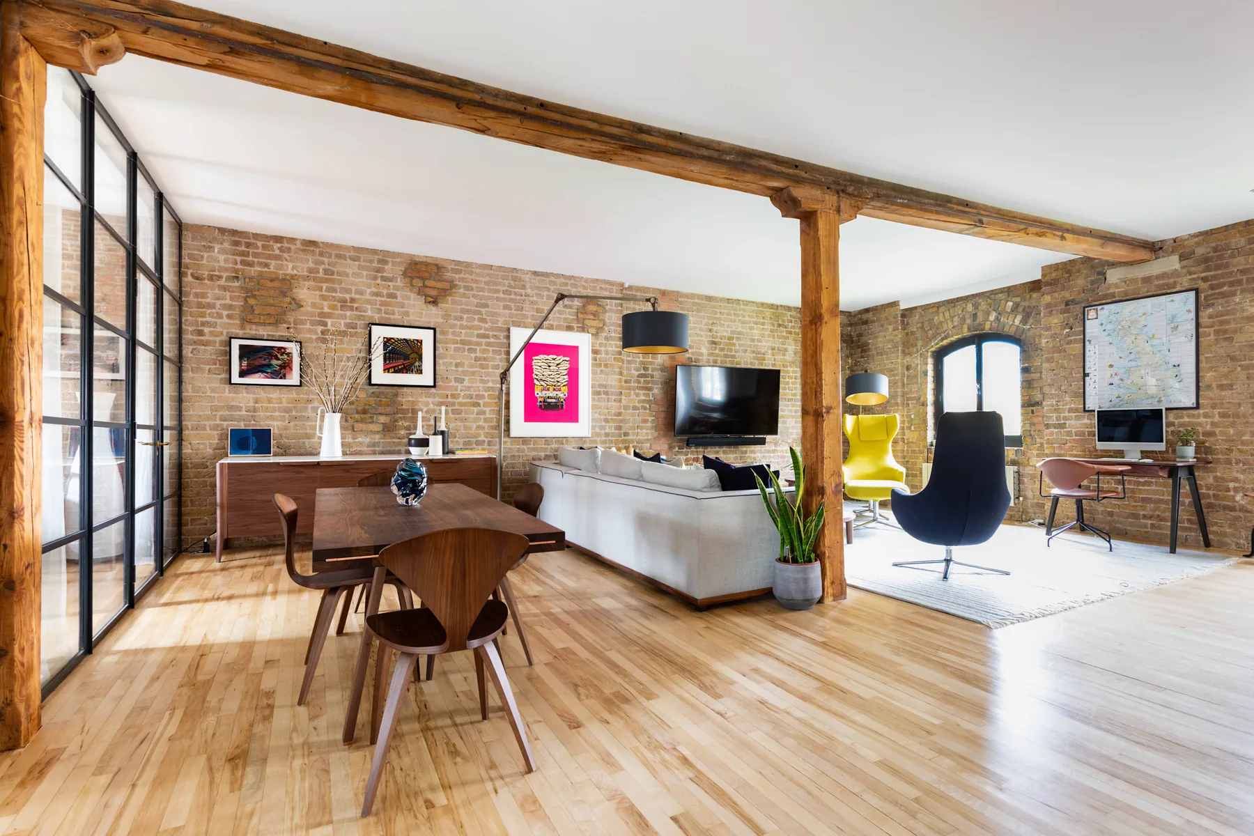A bright open-plan living and dining area with exposed brick walls and a wooden table.