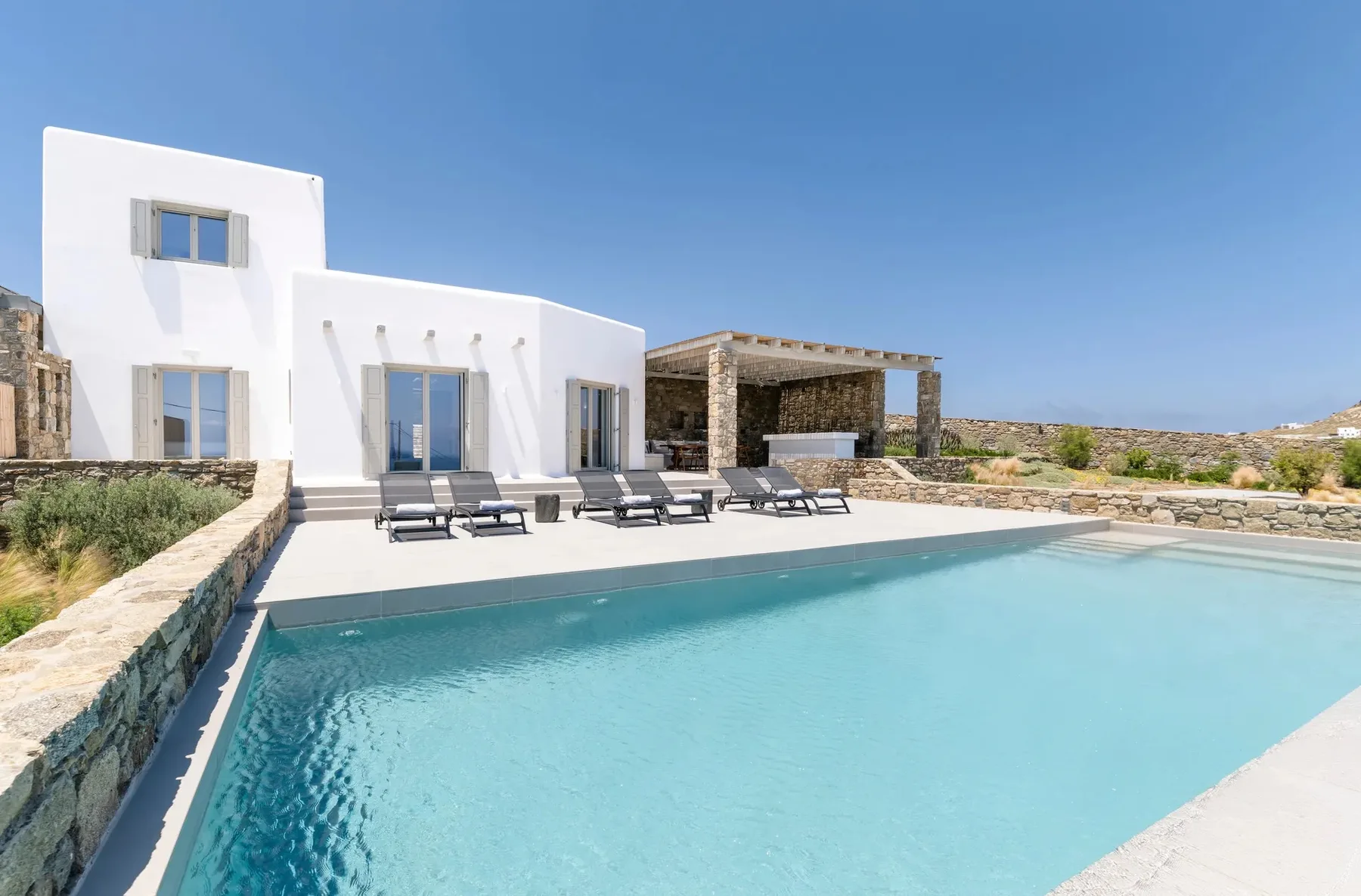 A swimming pool in front of a white modern villa under a clear sky.