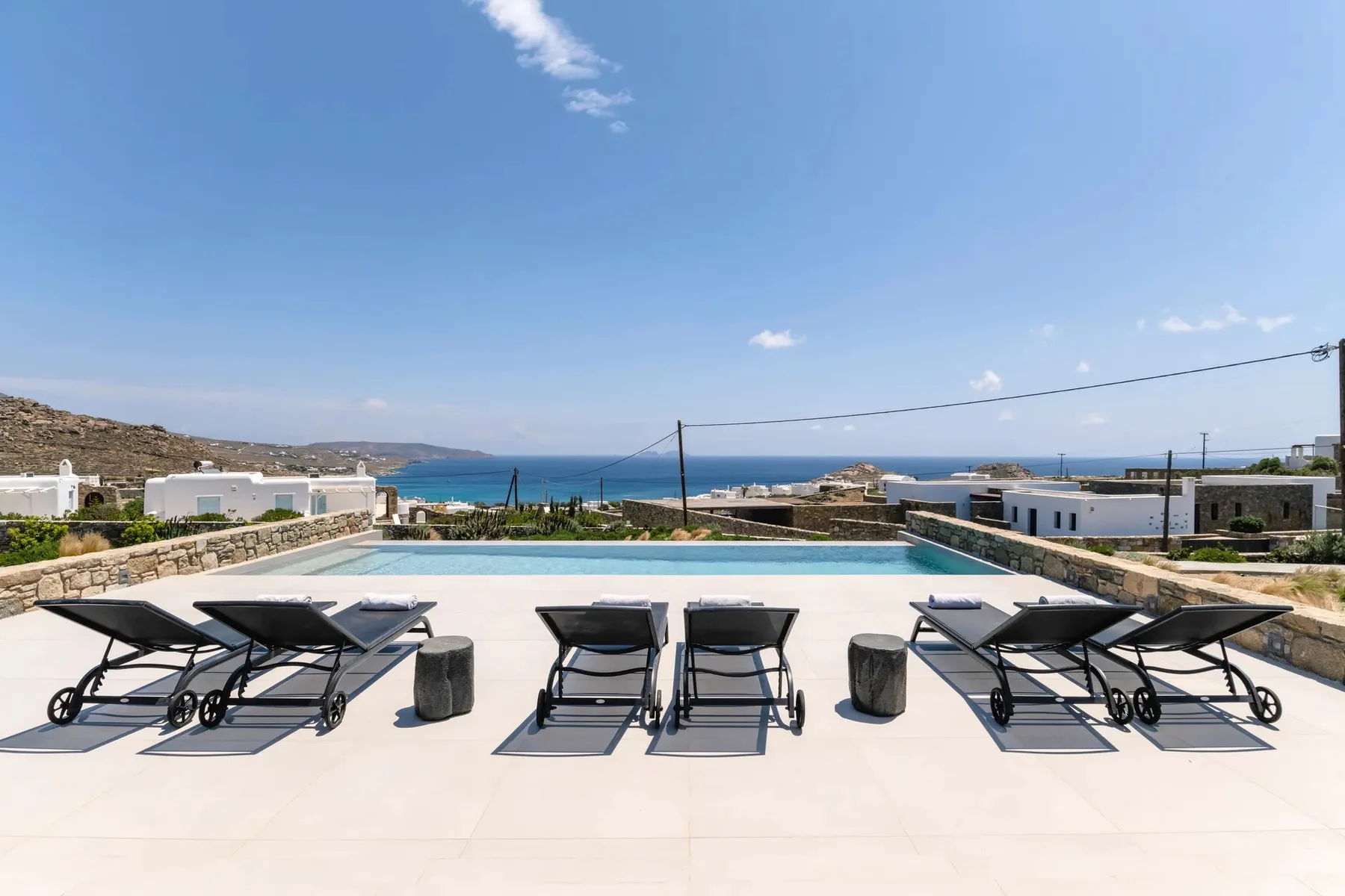 A sunlit pool terrace with lounge seating overlooks the sea.