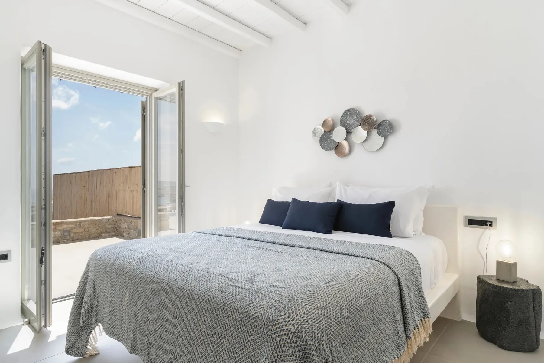 A bright bedroom with a double bed and open doors to an outdoor terrace.