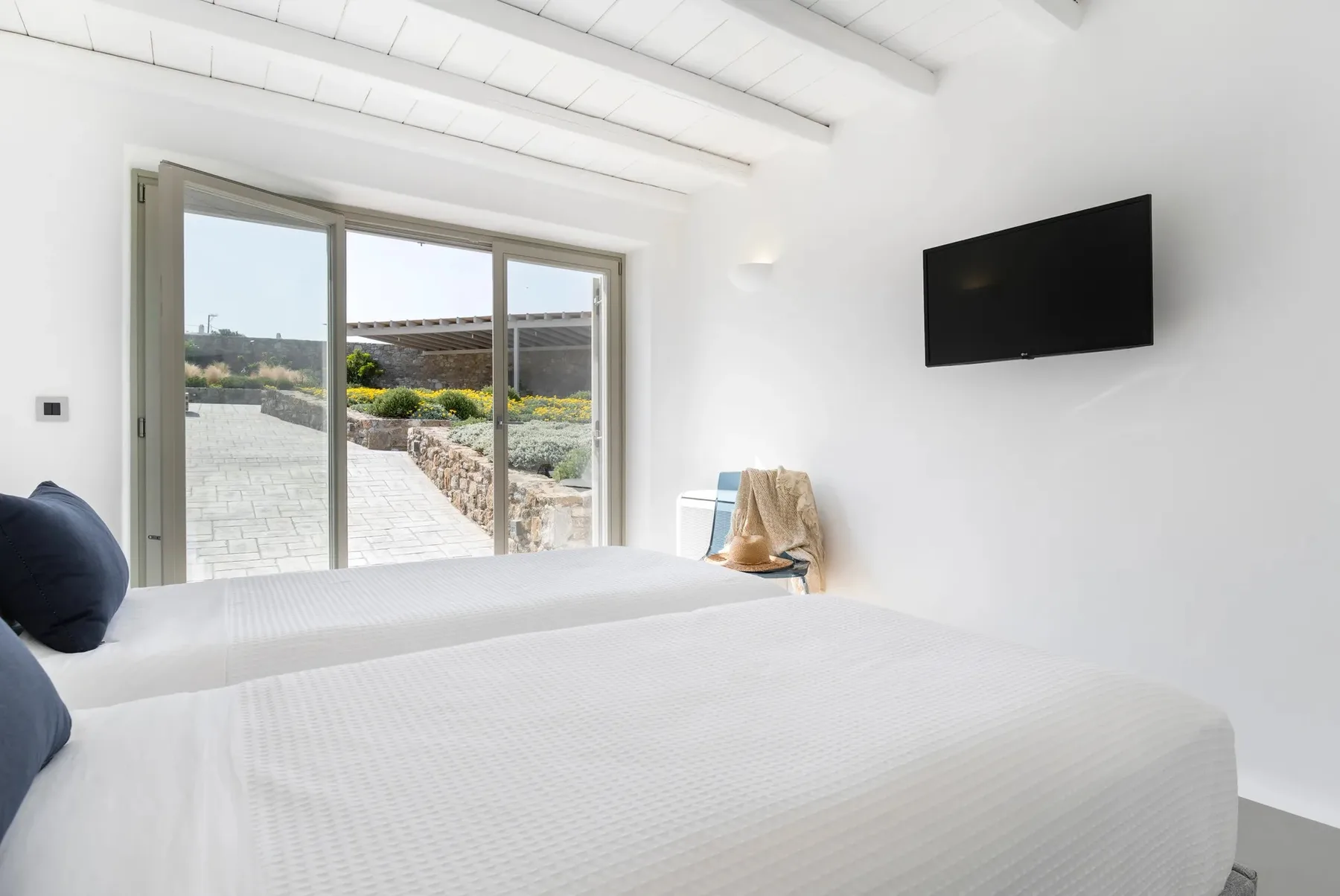 A bright bedroom with white bedding and sliding glass doors opening to a patio.
