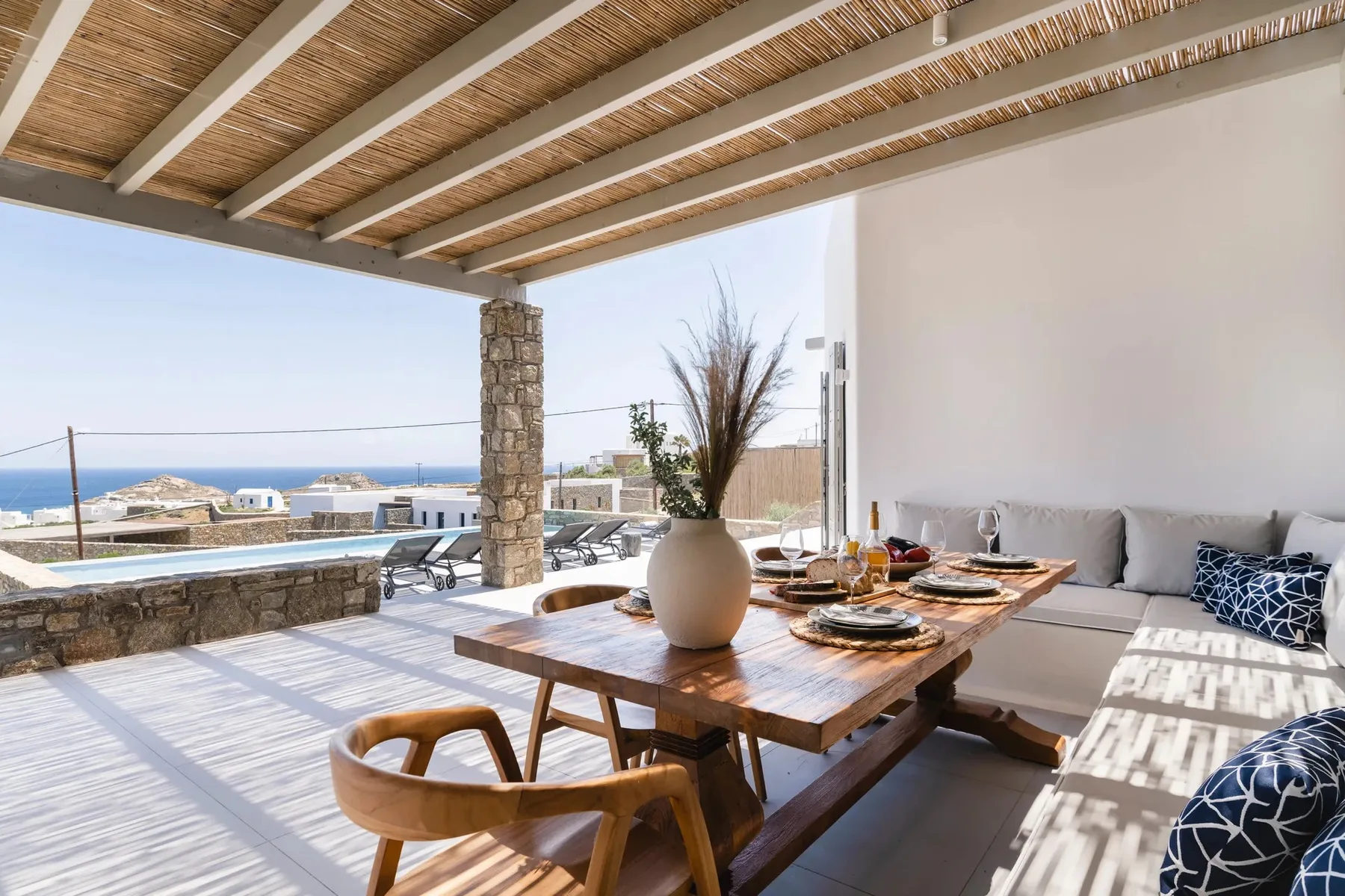 A covered terrace has a dining table, built-in seating, and a sea view.