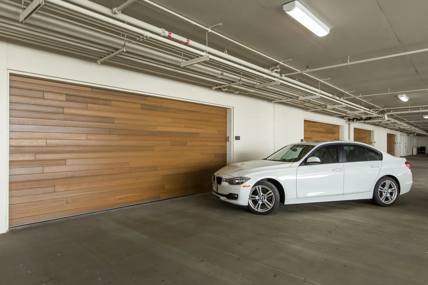An indoor parking garage with a white car parked beside wooden garage doors.
