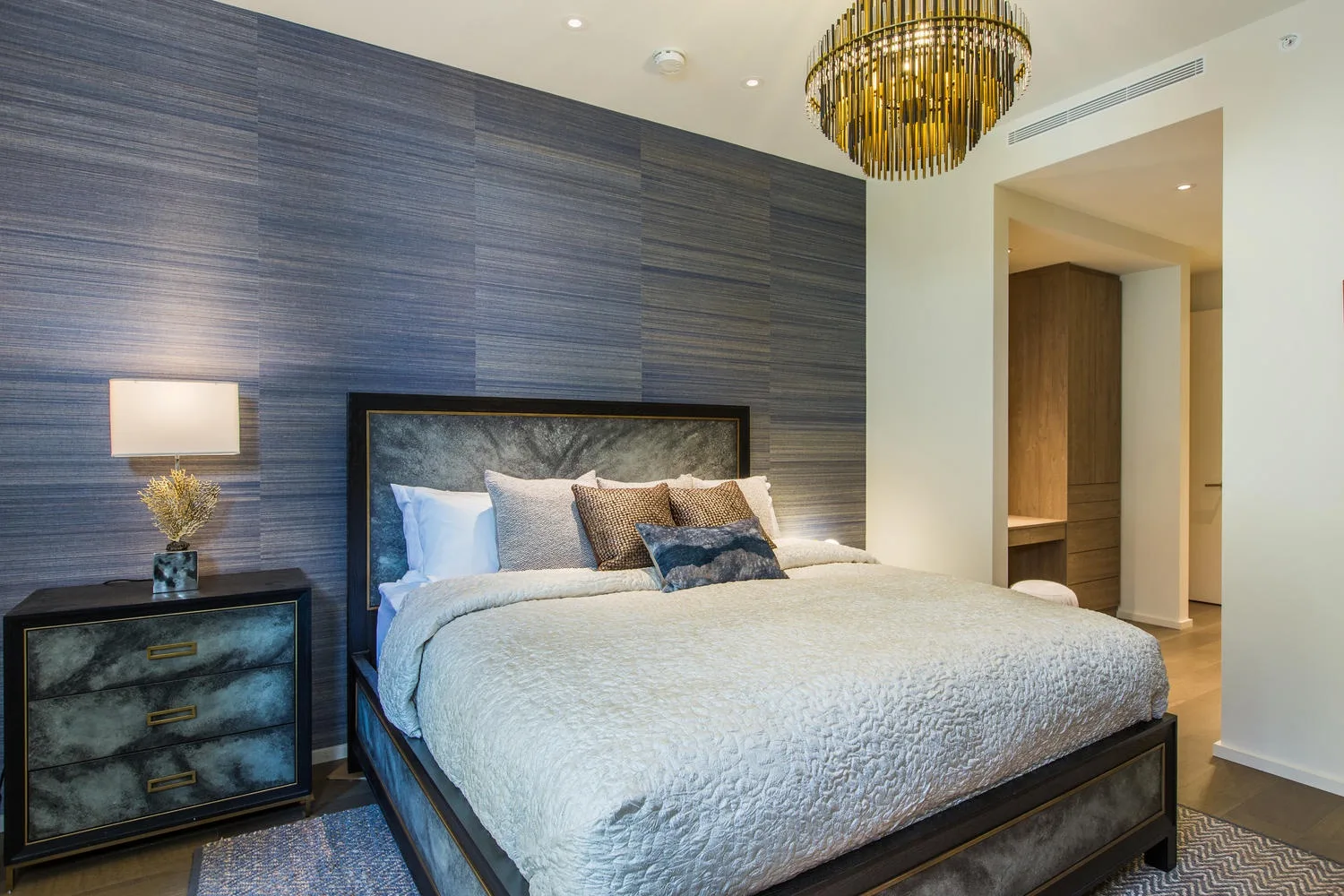A bedroom with a large bed against a dark textured wall.