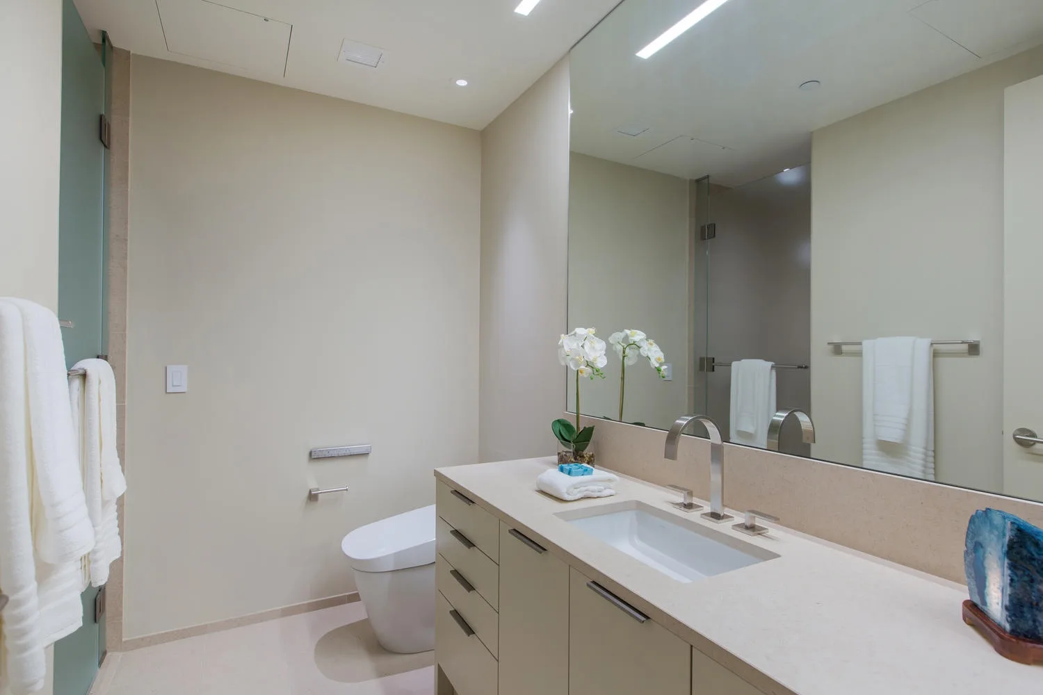 A bathroom with a long vanity, sink, mirror, and toilet.