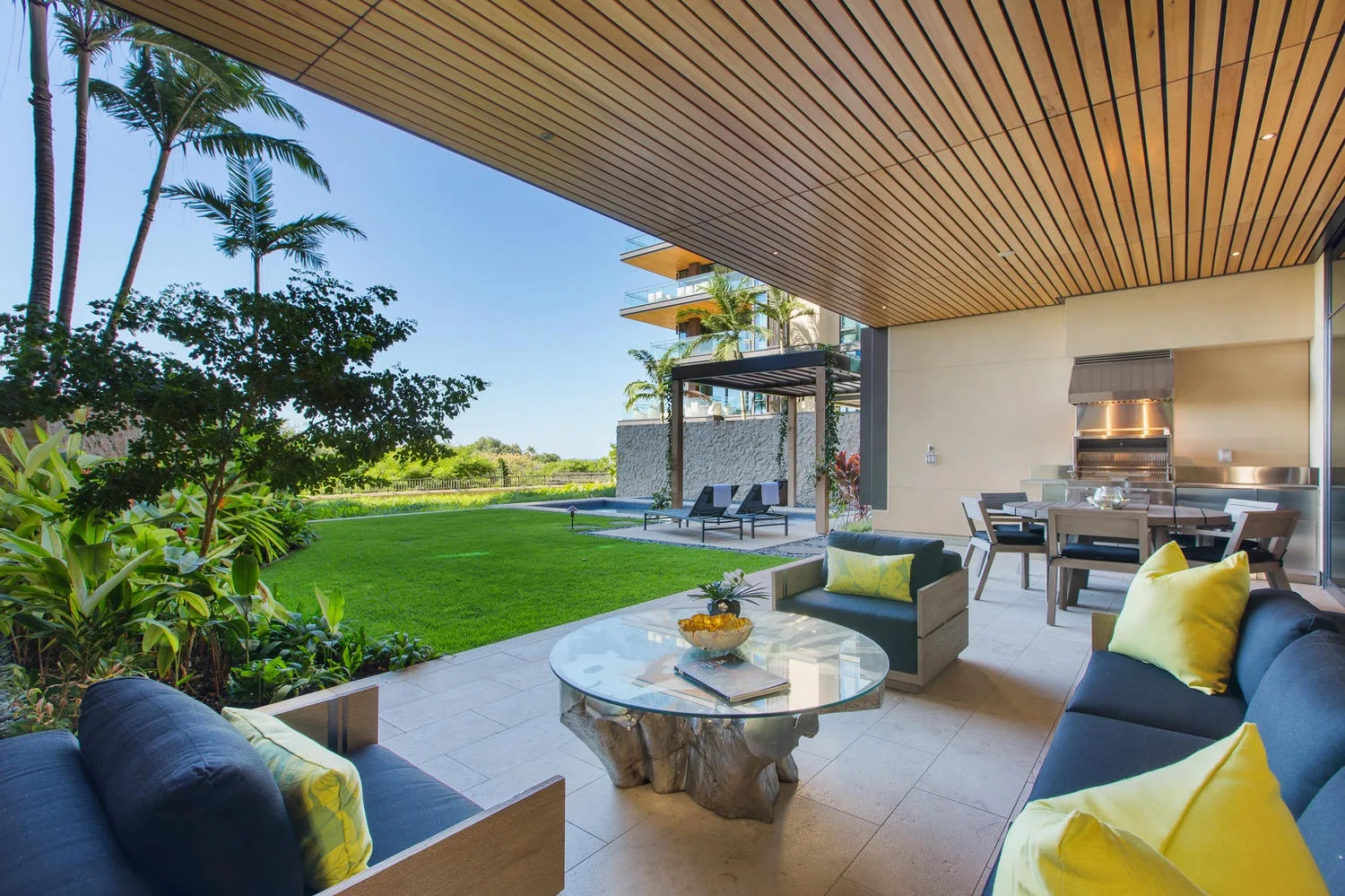 A covered patio with outdoor seating overlooks a green lawn and landscaped garden.