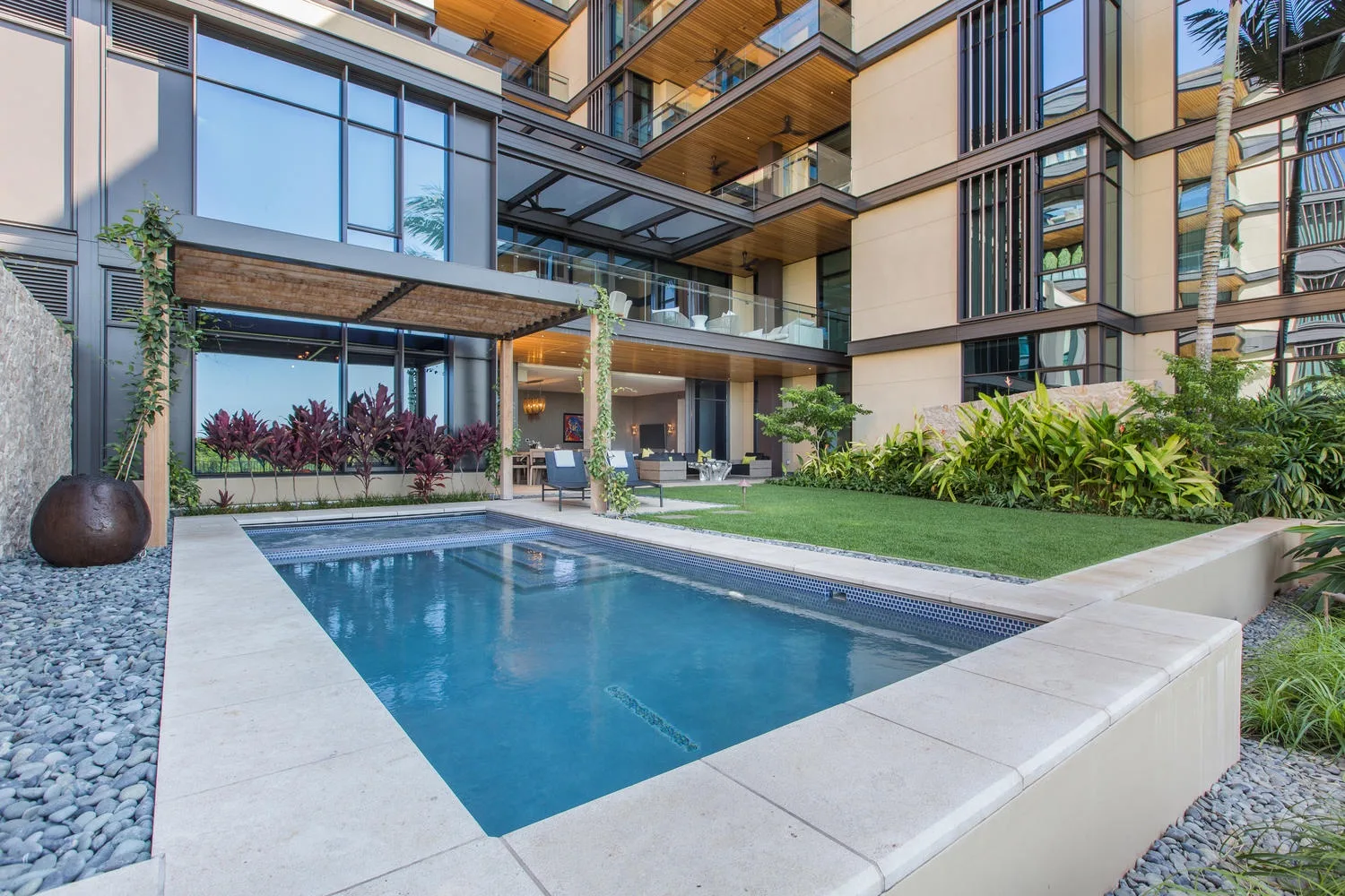 A courtyard pool sits beside a modern multi-story building and landscaped garden.