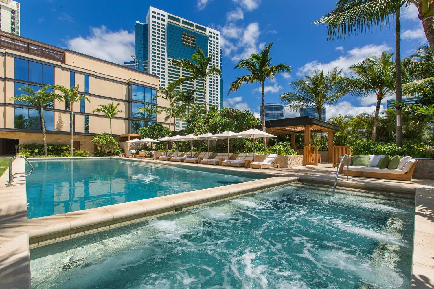 An outdoor pool and bubbling spa sit among palm trees and lounge seating.