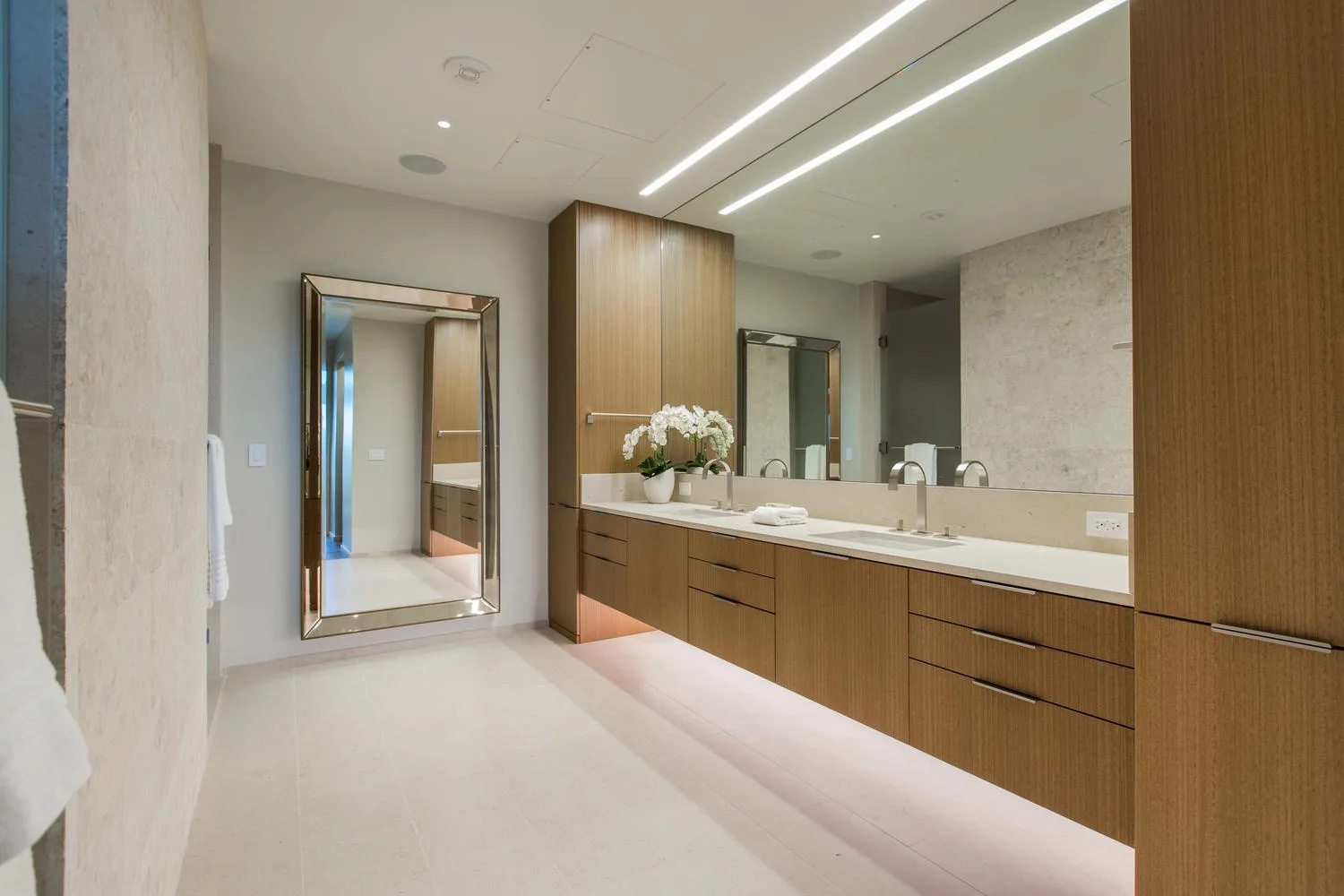 A modern bathroom with a long vanity, mirrors, and bright ceiling lights.