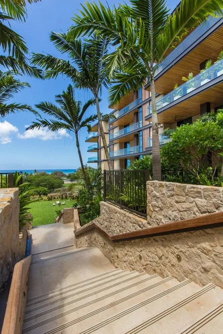 A landscaped walkway with steps leads toward a modern building and the sea.