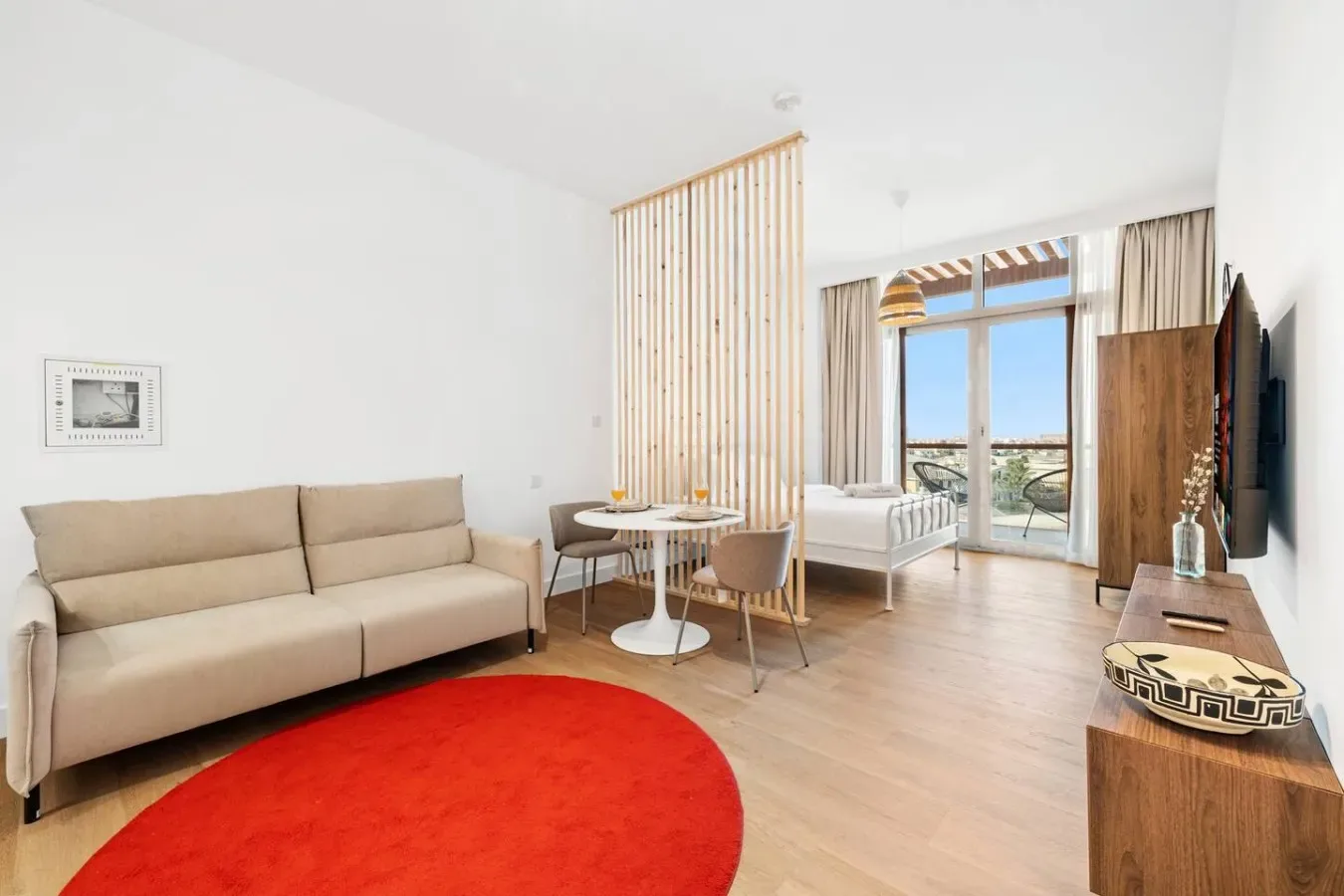 A bright living area with a beige sofa, round table, and red rug.