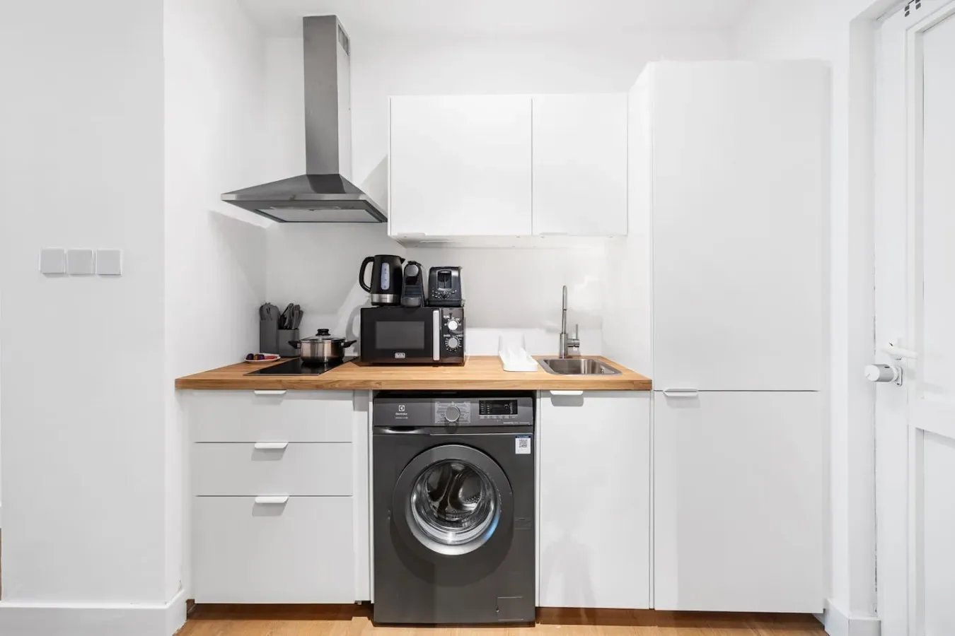 A compact white kitchen with a countertop, sink, and front-loading washing machine.