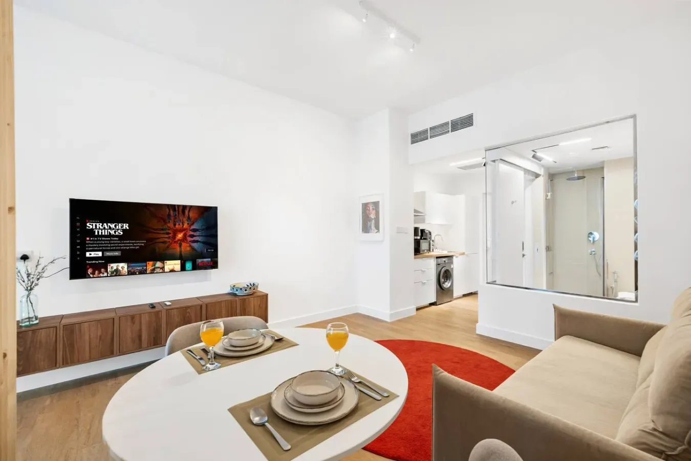 A bright living area has a dining table, seating, and a wall-mounted television.