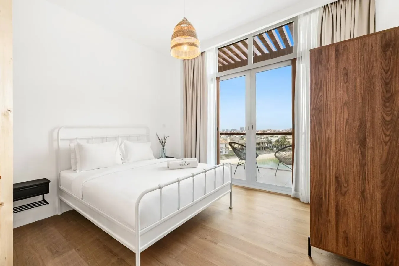 A bright bedroom with a white bed and glass doors opening onto a balcony.