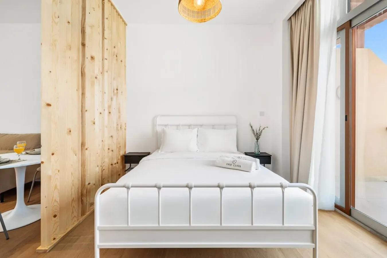 A bright bedroom with a white bed beside a large glass door.
