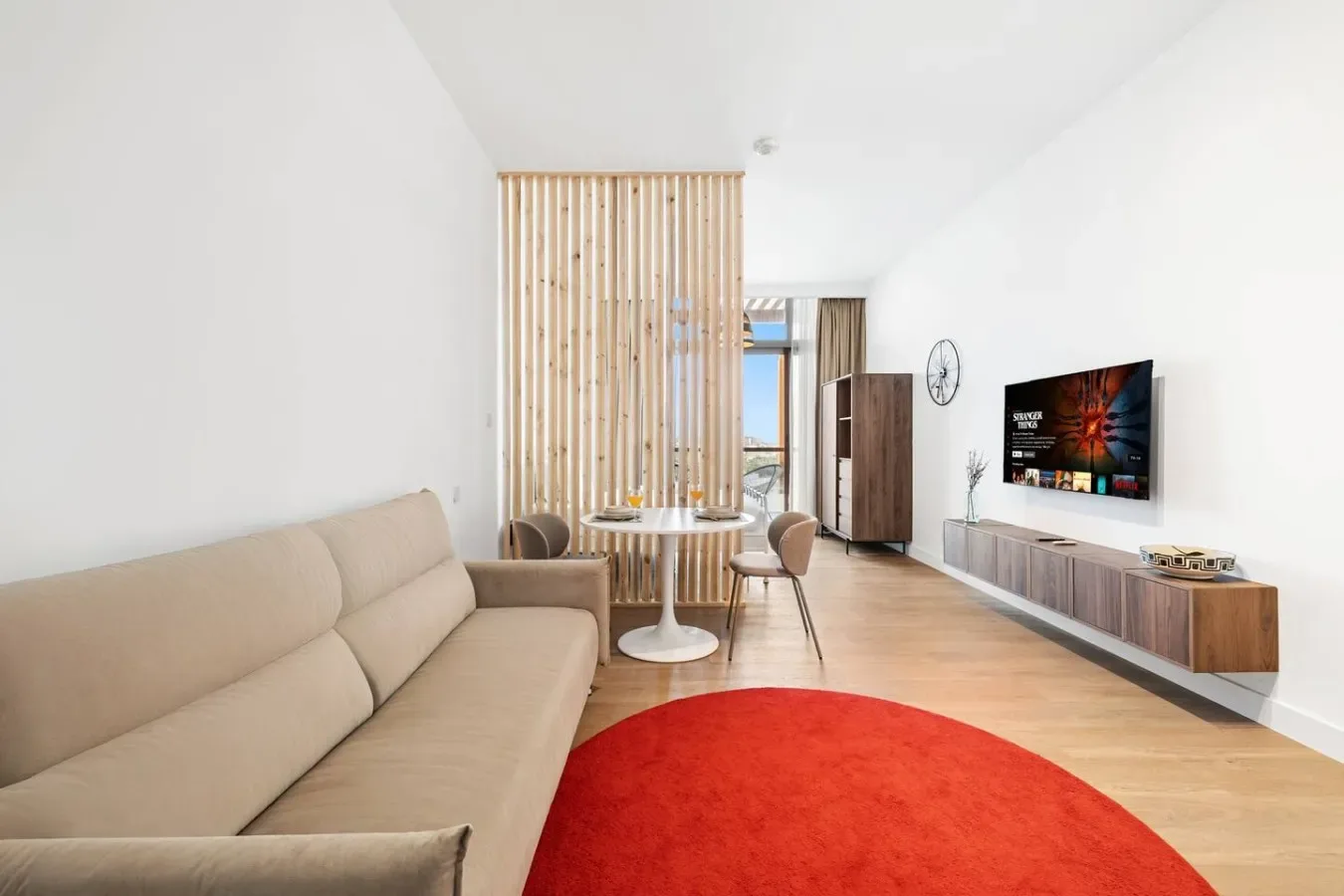 Una sala luminosa con zona de estar beige, mesa de comedor y alfombra roja.