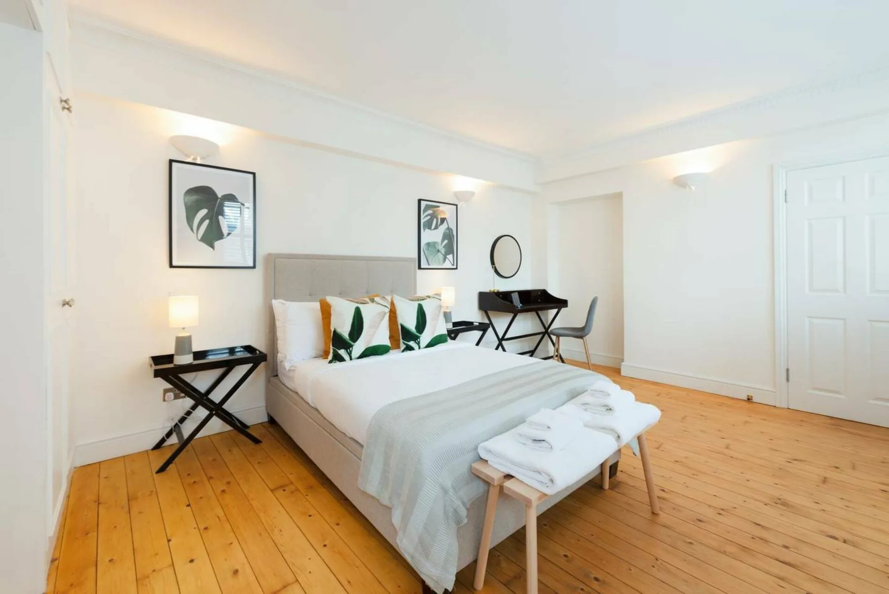 Un dormitorio luminoso con una cama tendida y cuadros en las paredes.