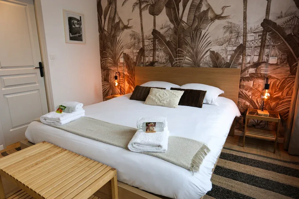 A bedroom with a neatly made bed beneath a tropical mural.