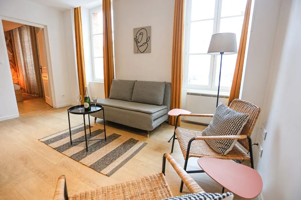 A bright living room with a gray sofa, patterned rug, and woven seating.