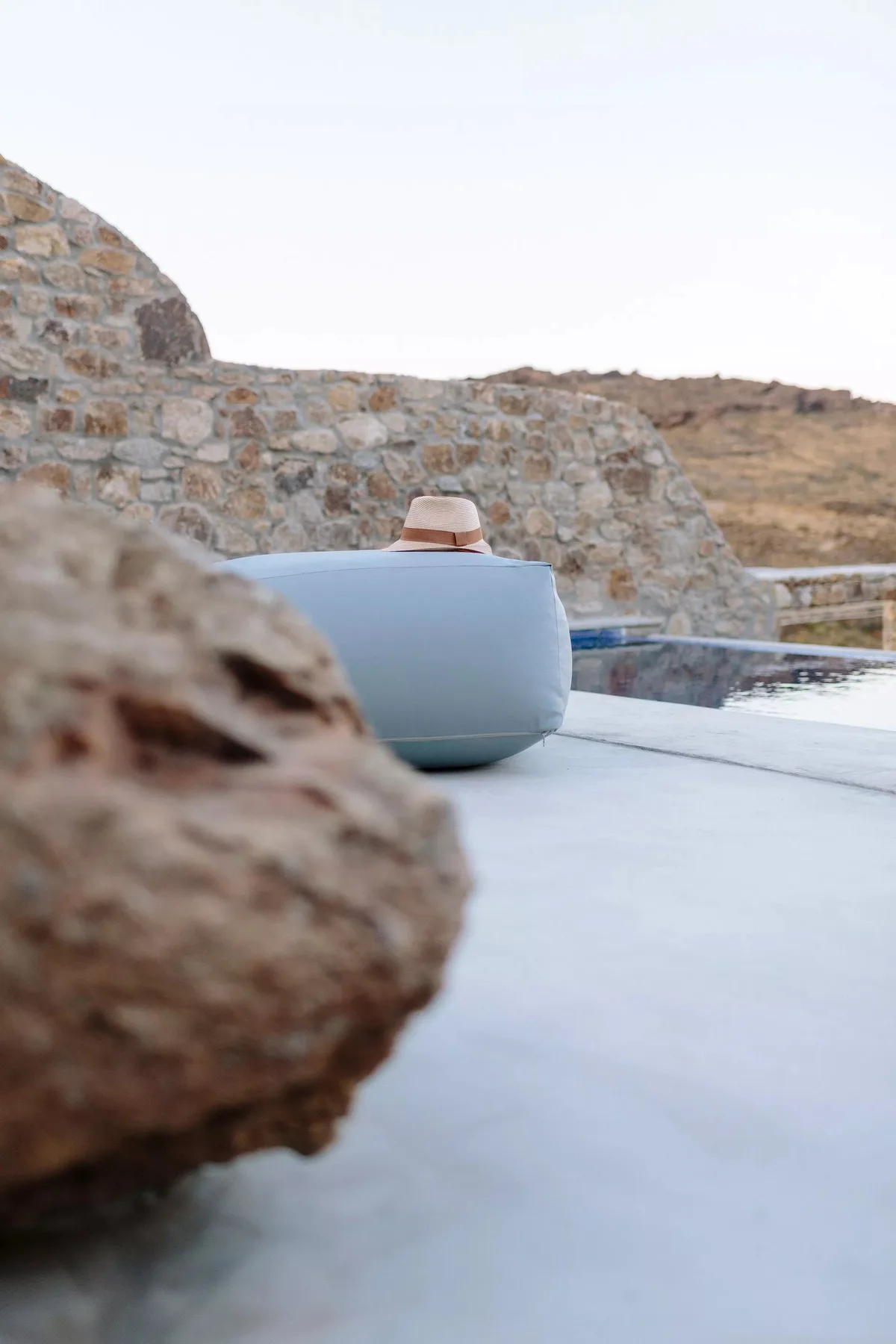 An outdoor pool with a light-colored lounge seat beside a stone wall.