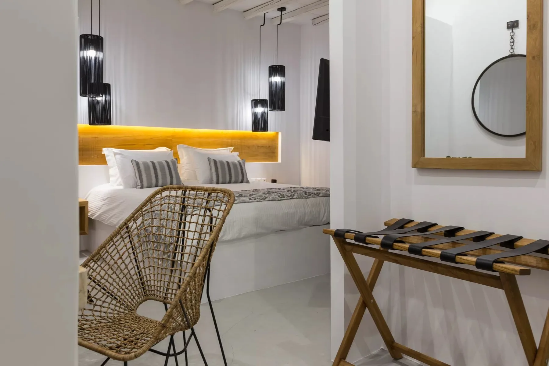 A bedroom with a bed, hanging pendant lights, and a woven chair.