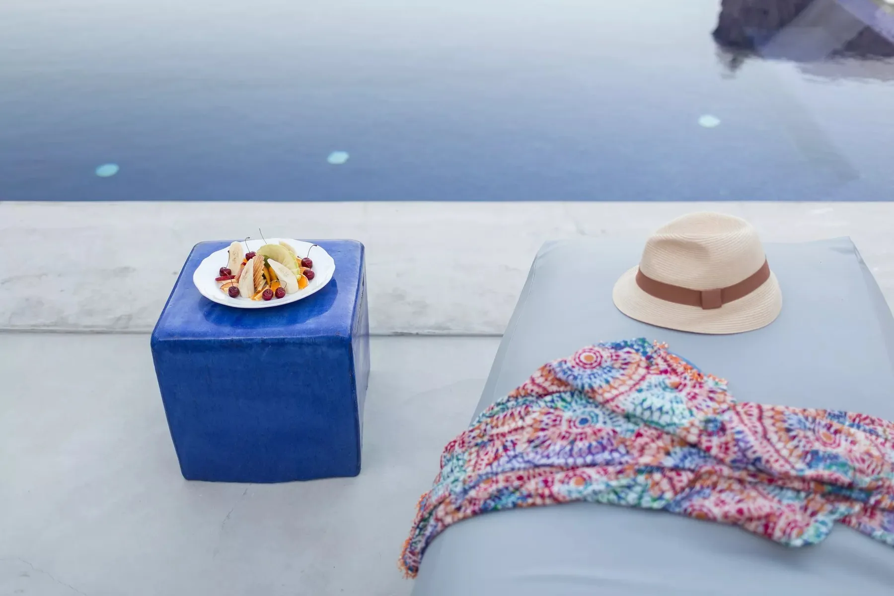 A colorful cover-up and sun hat rest beside a pool.