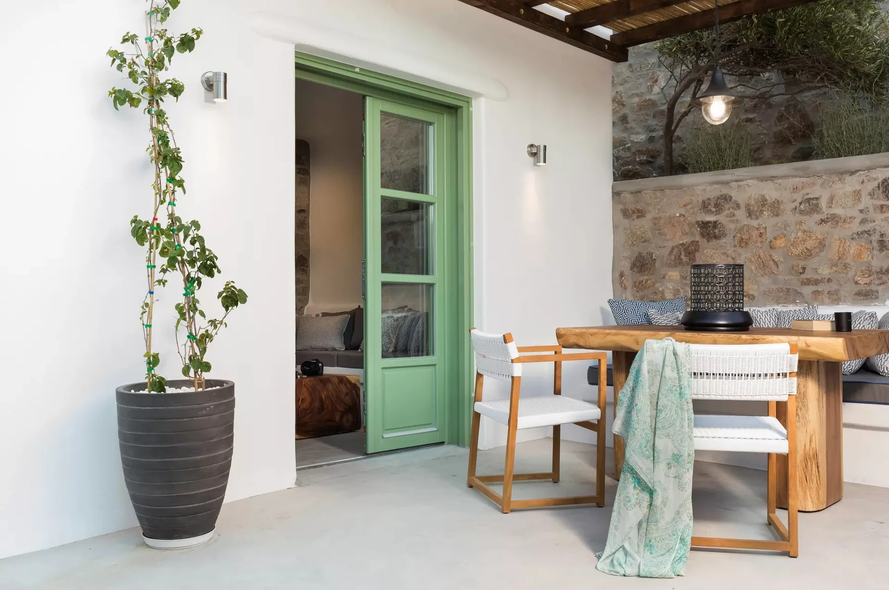 A patio dining area with a wooden table beside a green-framed doorway.