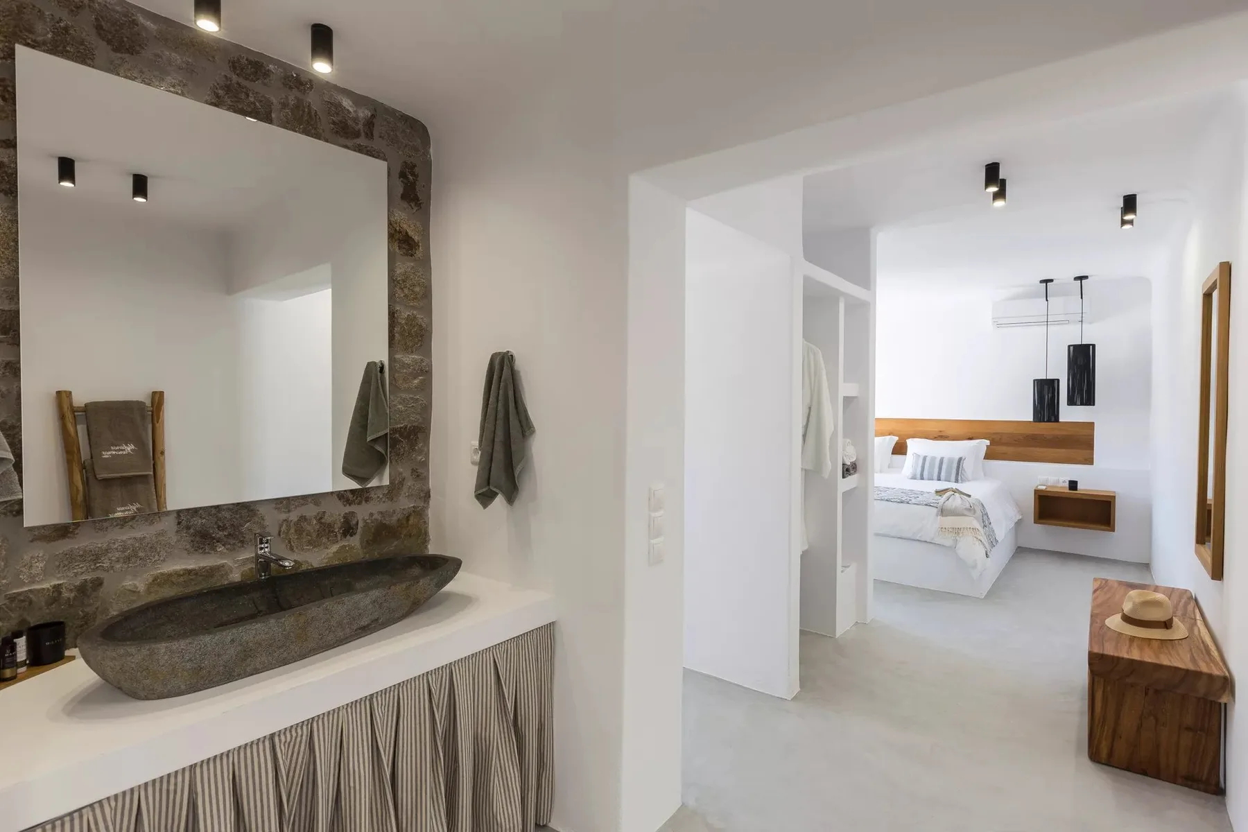 A bathroom vanity opens onto a bedroom with a neatly made bed.