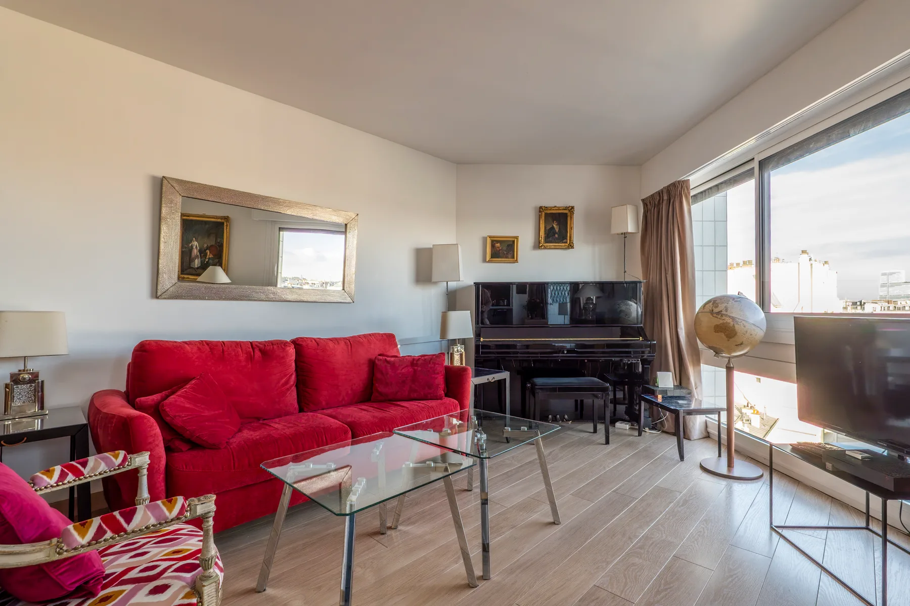 A bright living room with red seating, a glass coffee table, and a television.