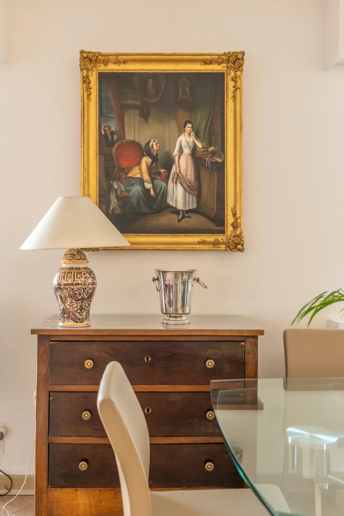 A dining area with a wooden chest of drawers beneath a framed painting.