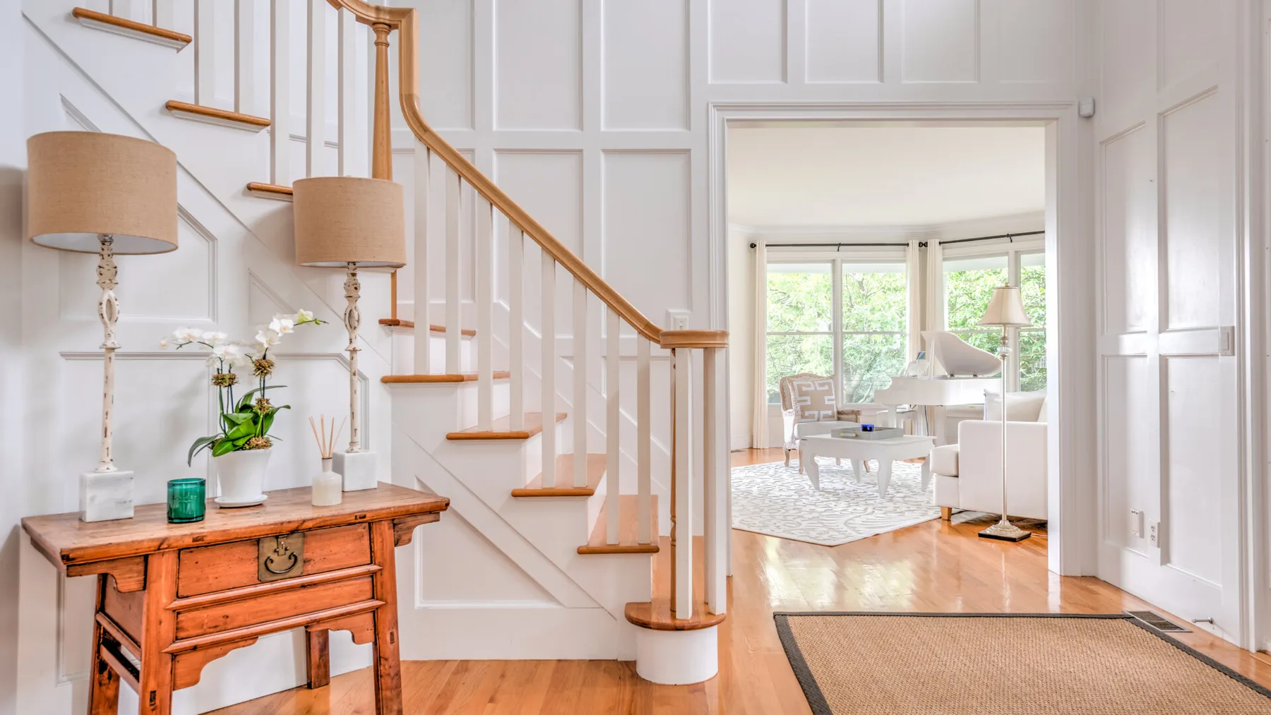 Un pasillo interior luminoso con una escalera de madera que conduce a una sala de estar soleada.