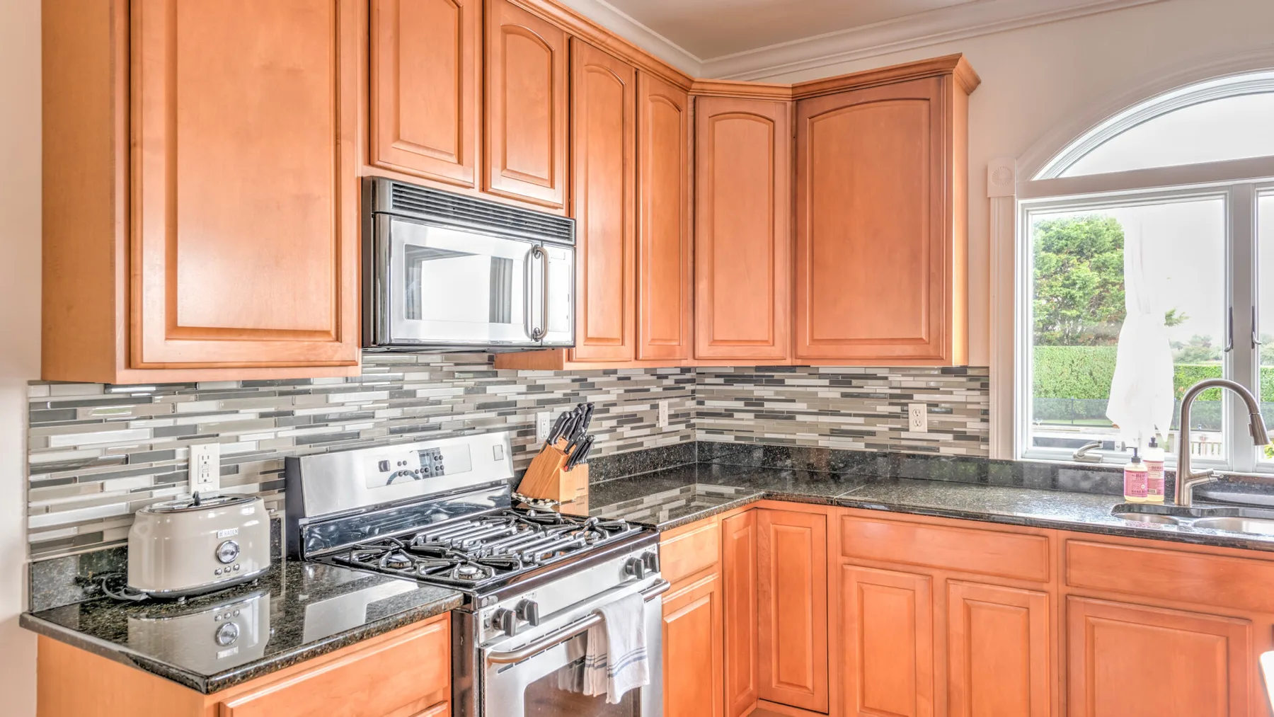 A kitchen with wood cabinets, a stove, and a window overlooking greenery.