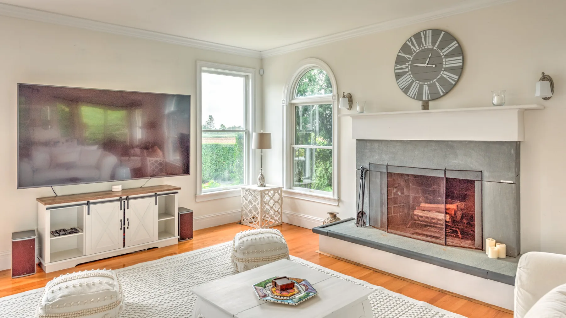 A bright living room with a fireplace, television, and large windows.