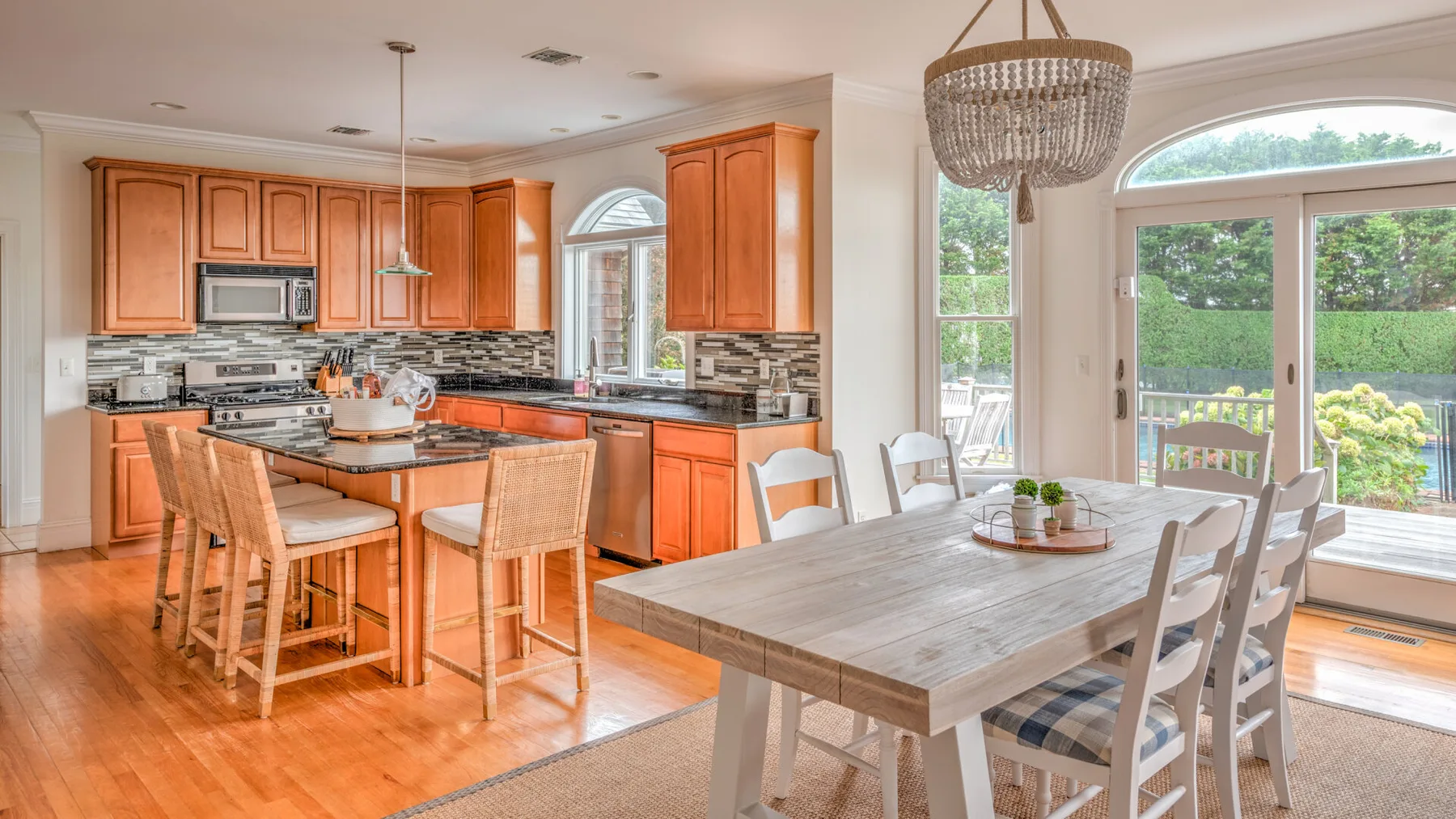 Una luminosa cocina con comedor, gabinetes de madera y una mesa junto a puertas de vidrio.