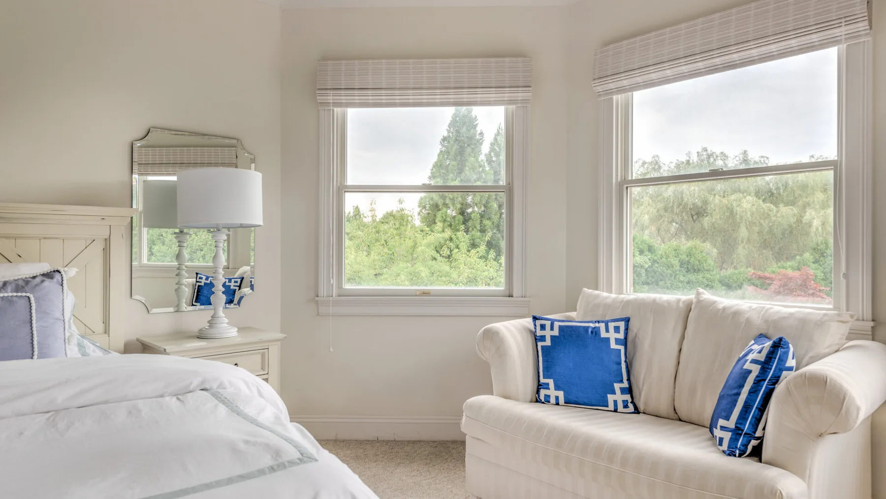 Un dormitorio luminoso con una cama y un sofá blanco junto a dos ventanas.