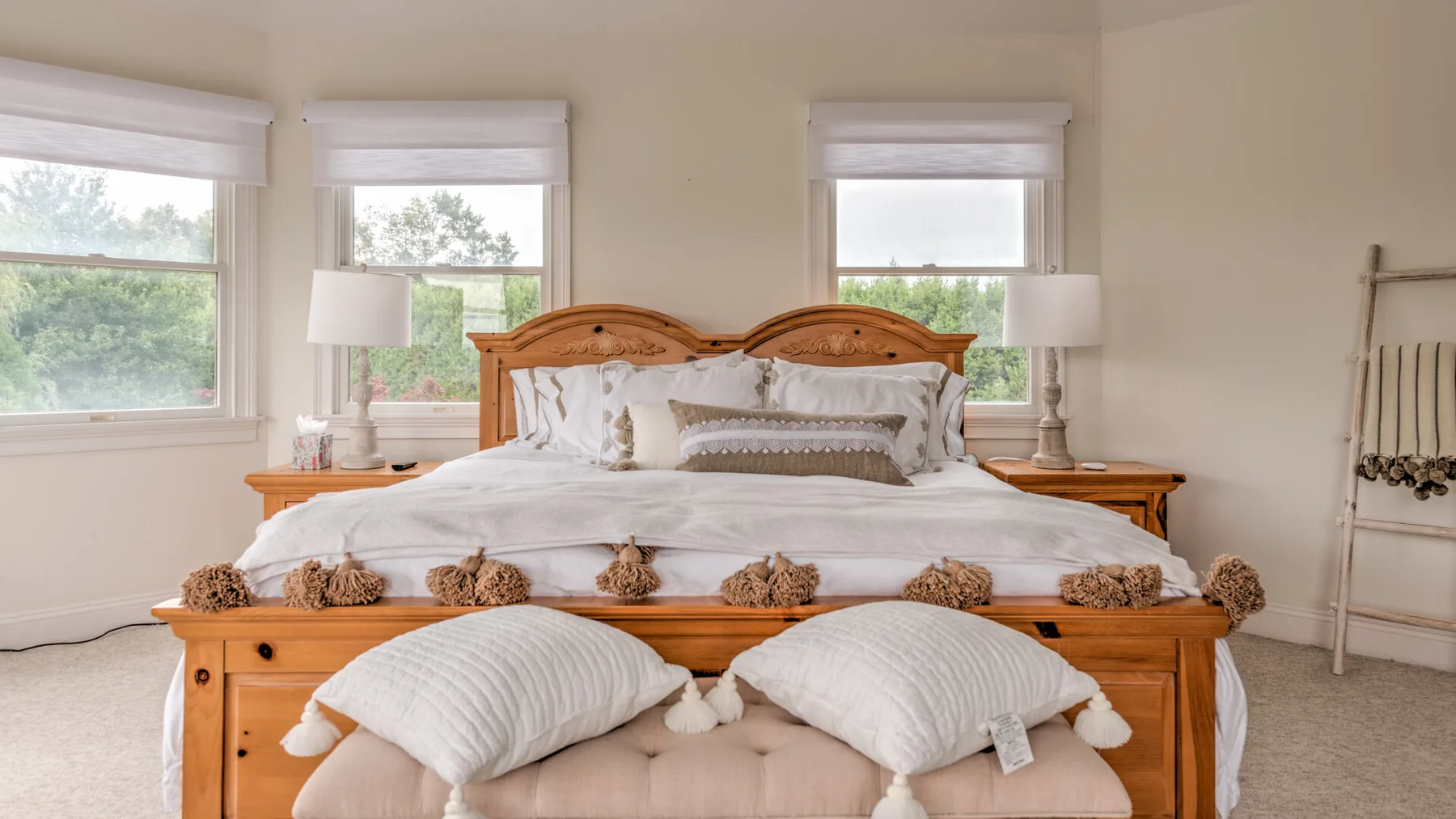 Un dormitorio con una cama de madera, ropa de cama blanca y dos ventanas.