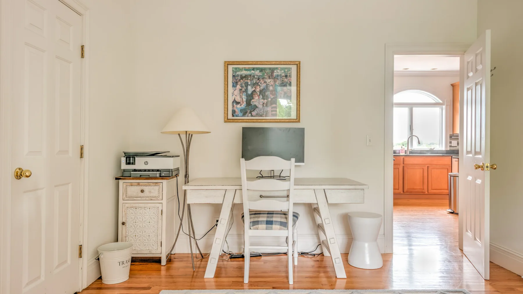 Una habitación luminosa con escritorio, computadora y una puerta abierta hacia la cocina.