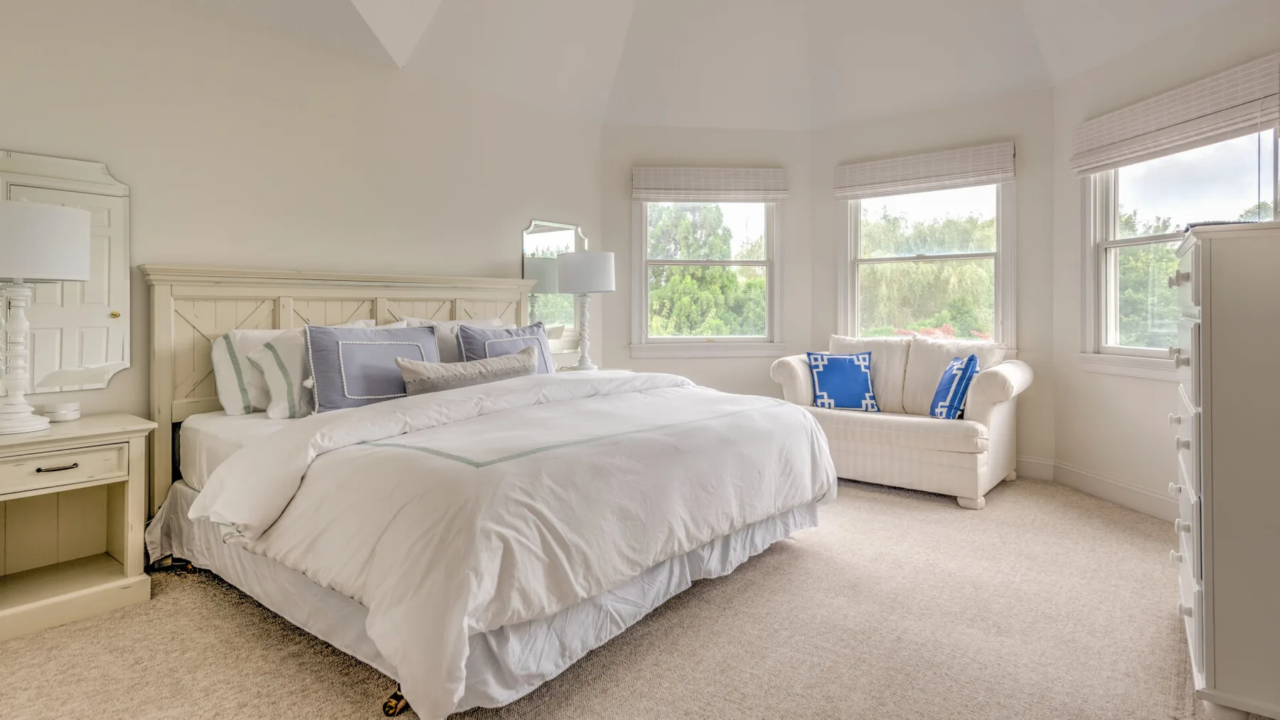 Un dormitorio luminoso con una cama grande y una zona de estar junto a las ventanas.