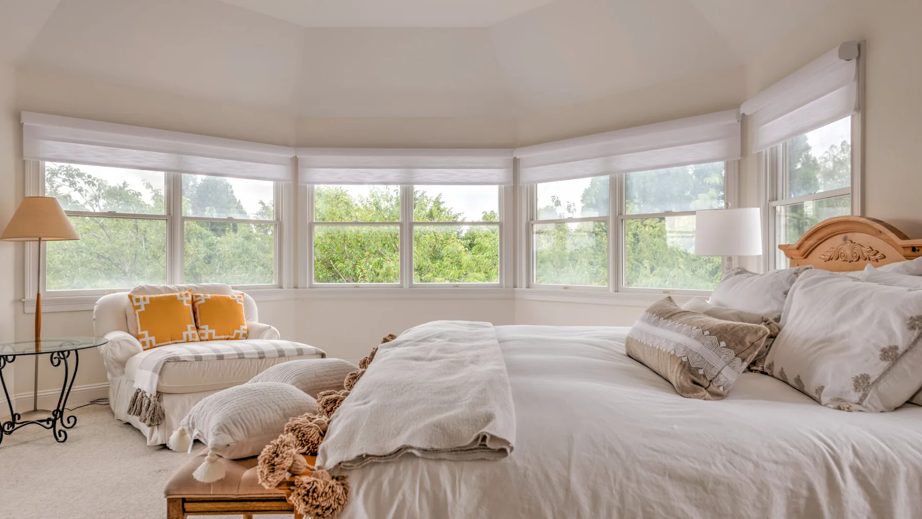 Un dormitorio luminoso con una cama grande y varias ventanas con vistas a la vegetación.