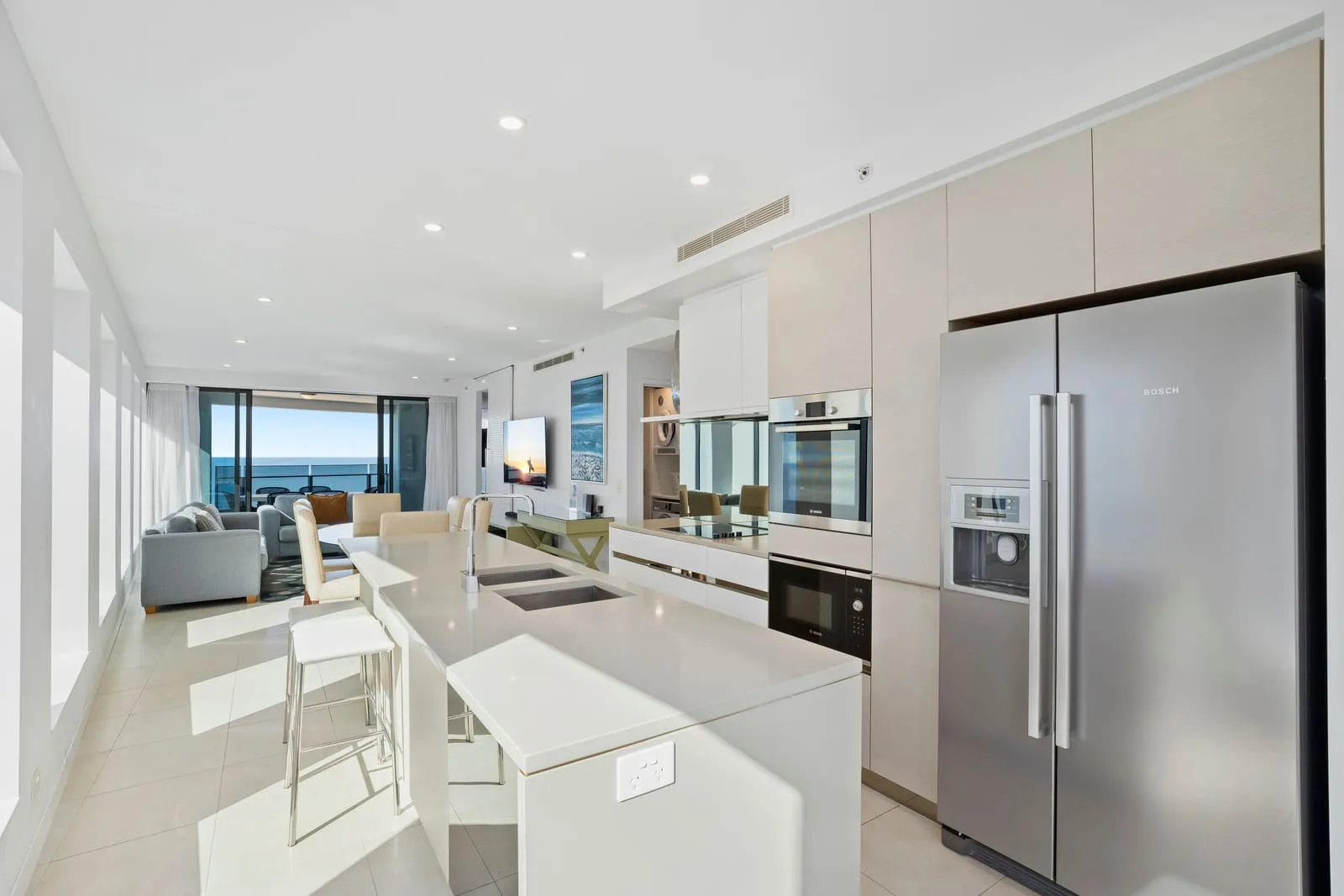 Una cocina abierta al salón, con una isla y el océano visible por las ventanas.