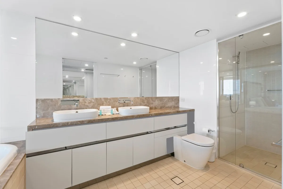 Un baño luminoso con un mueble largo, dos lavabos y una ducha de vidrio.