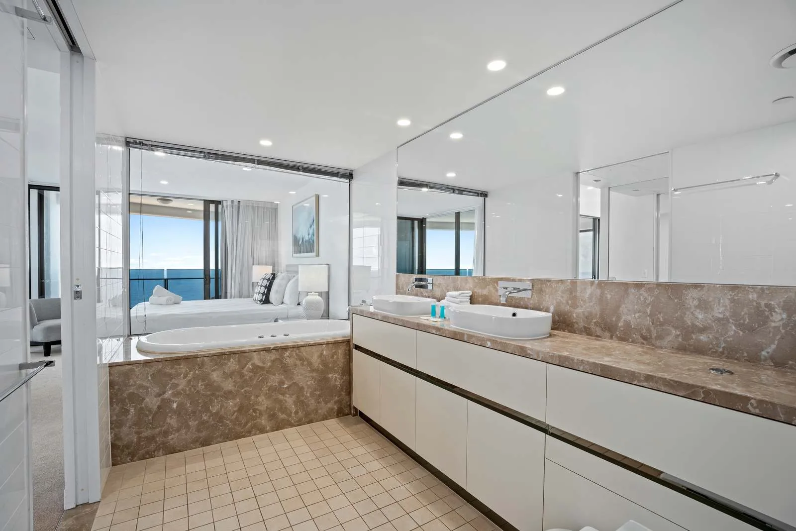 Un baño luminoso con un lavabo largo y una bañera con vistas al océano.