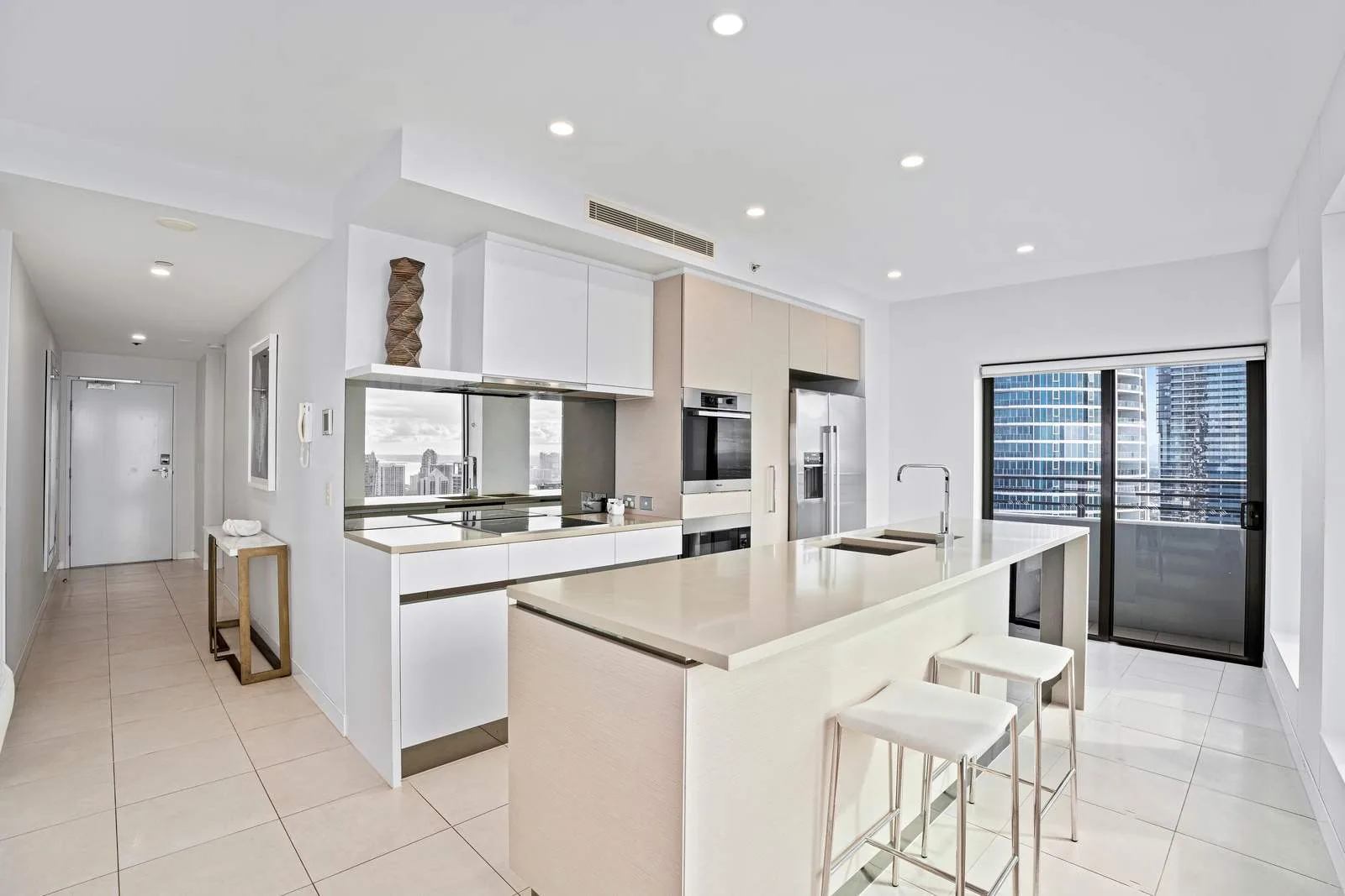 Una cocina moderna y luminosa con isla y taburetes junto a grandes ventanas.