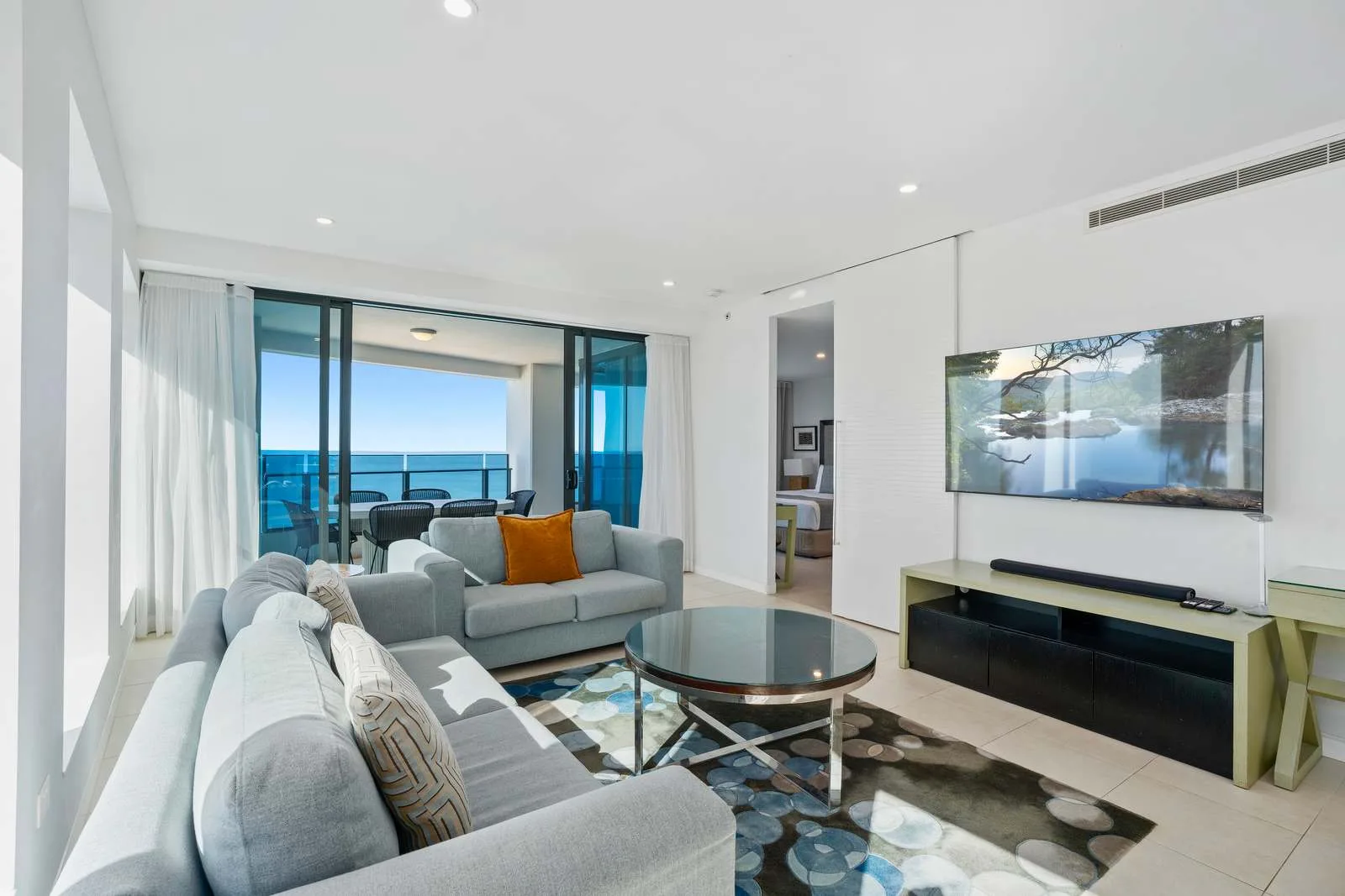 Una sala luminosa tiene asientos grises, una mesa de centro redonda y puertas corredizas de vidrio.