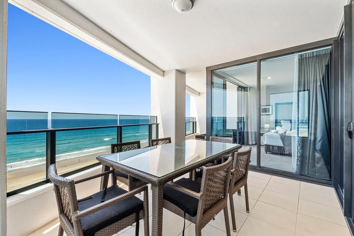 Un balcón cubierto tiene una mesa de comedor y asientos junto al mar.